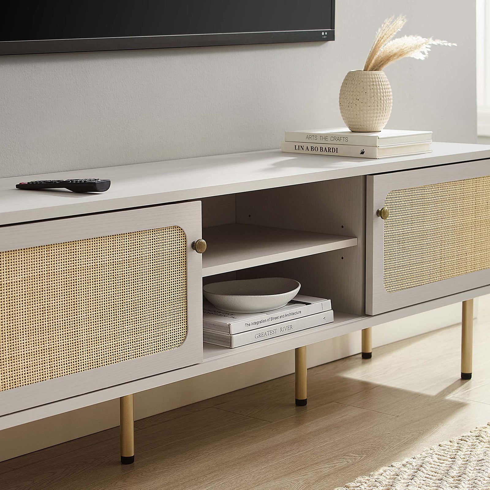 White rattan TV stand styled beneath a wall-mounted TV with books and decor in a light-filled room. || EEI-6045-WHI || storage_room