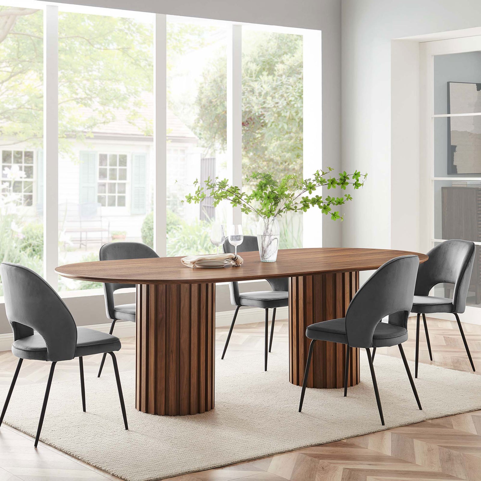 Walnut oval dining table with fluted columns styled in a bright modern dining room with four upholstered chairs || EEI-6065-WAL-SET || front_angle_room