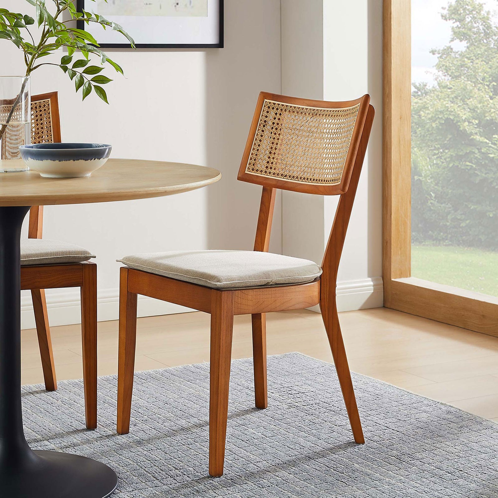 Walnut and beige upholstered dining chair beside a round pedestal table in a sunlit modern dining space. || EEI-6080-WAL-BEI || front_angle_room