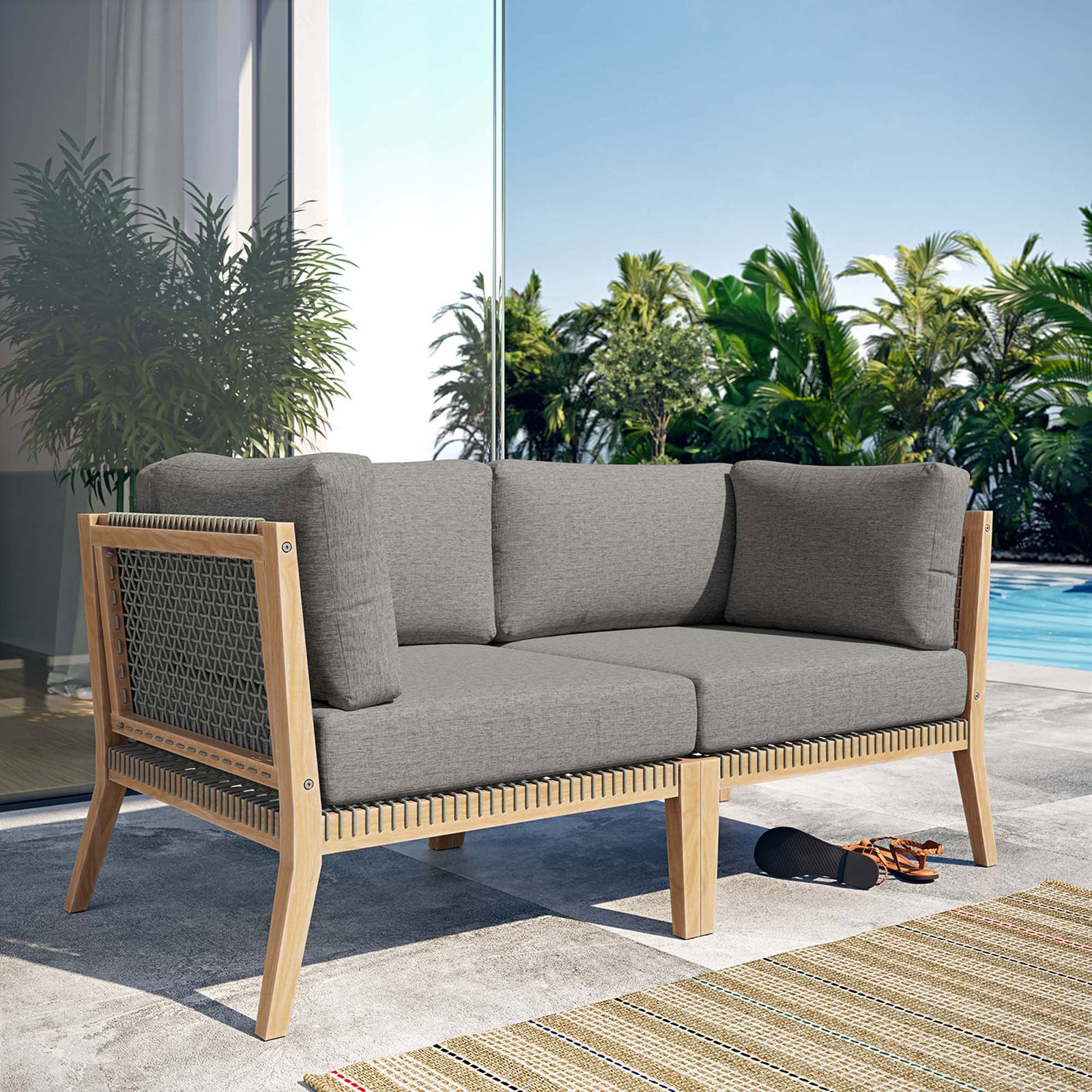 Clearwater teak loveseat with gray graphite cushions styled on a sunlit poolside patio || EEI-6119-GRY-GPH || front_angle_room