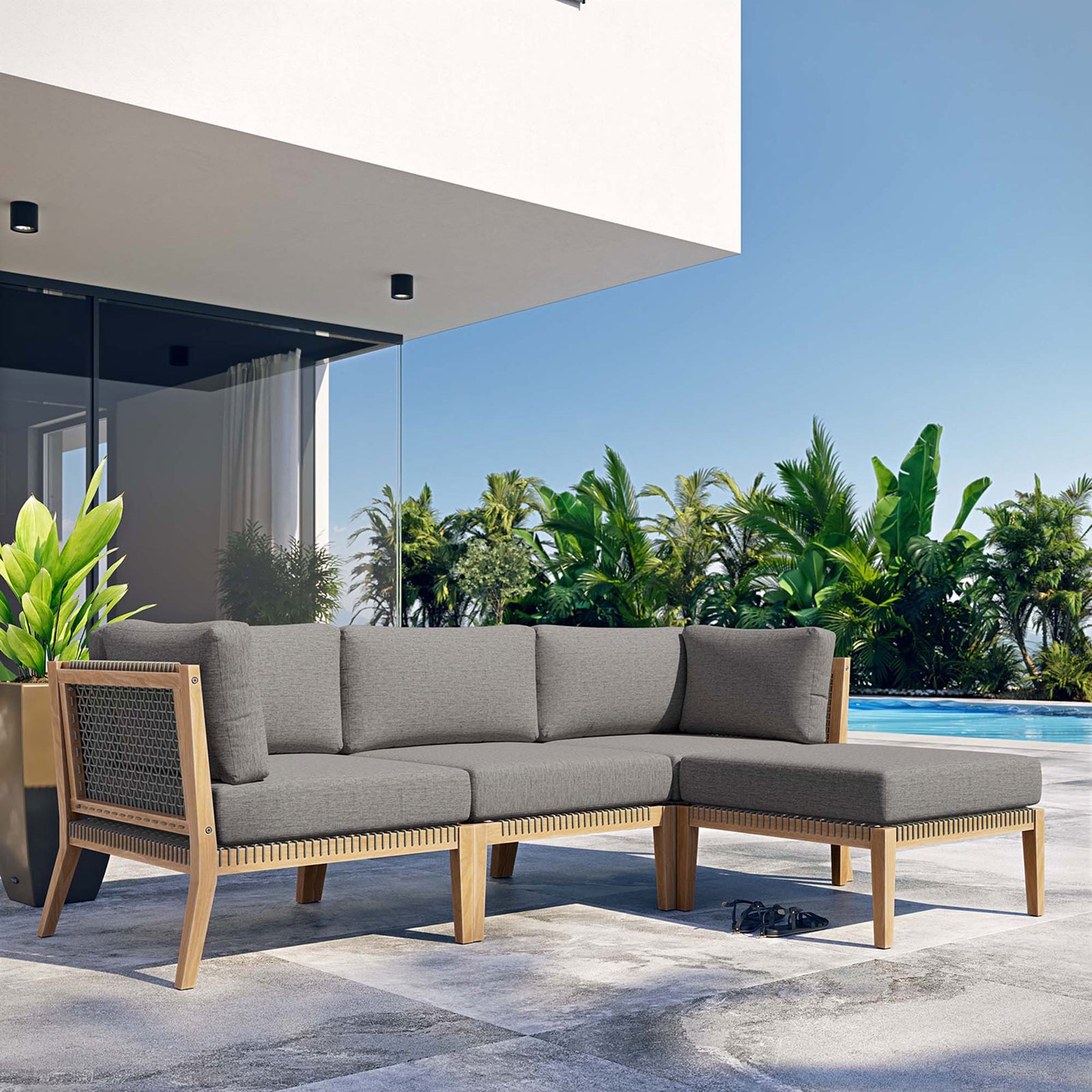 Graphite gray teak sectional sofa by the pool framed by palm trees and modern architecture || EEI-6121-GRY-GPH || front_angle_room