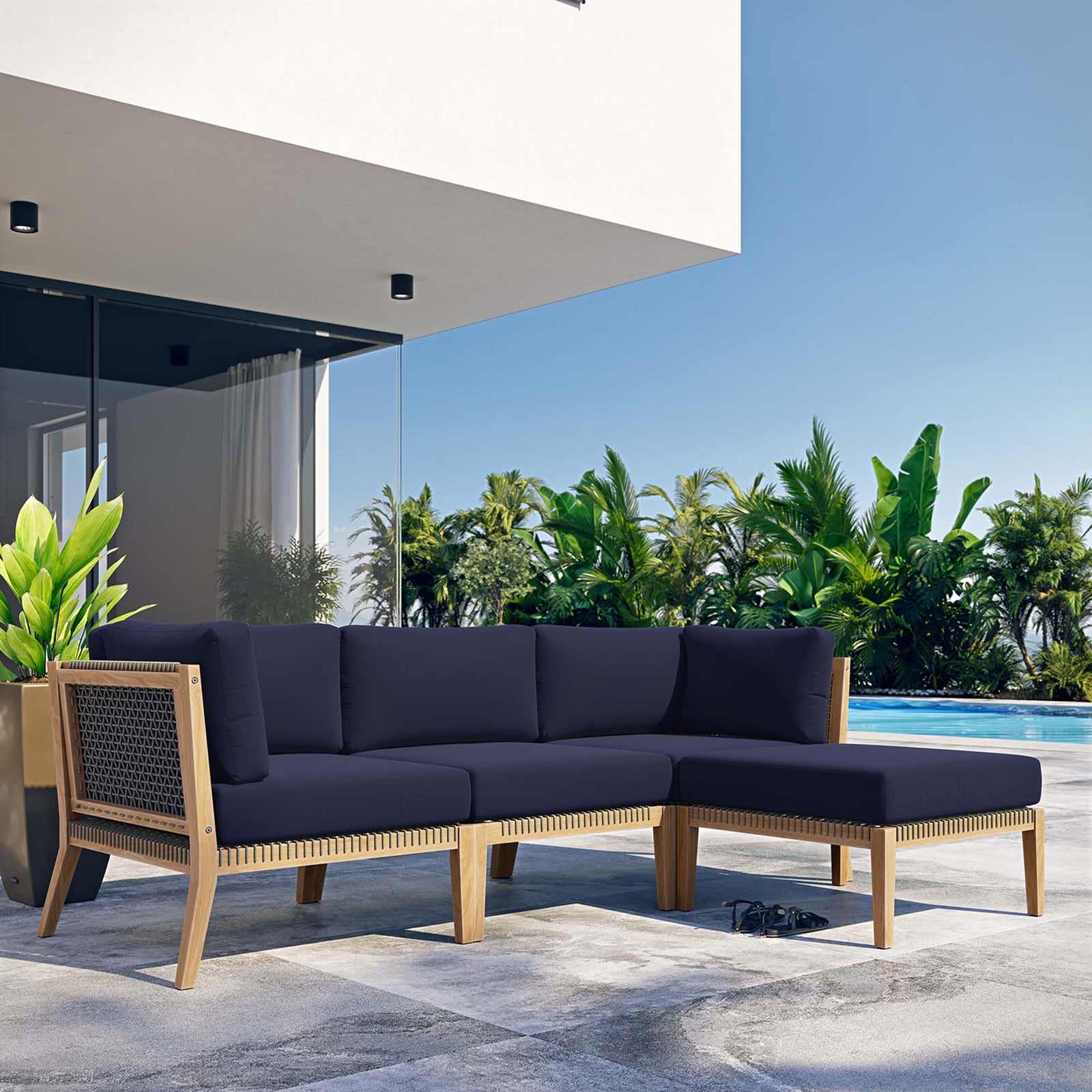Navy blue teak sectional sofa by the pool framed by palm trees and modern architecture || EEI-6121-GRY-NAV || front_angle_room