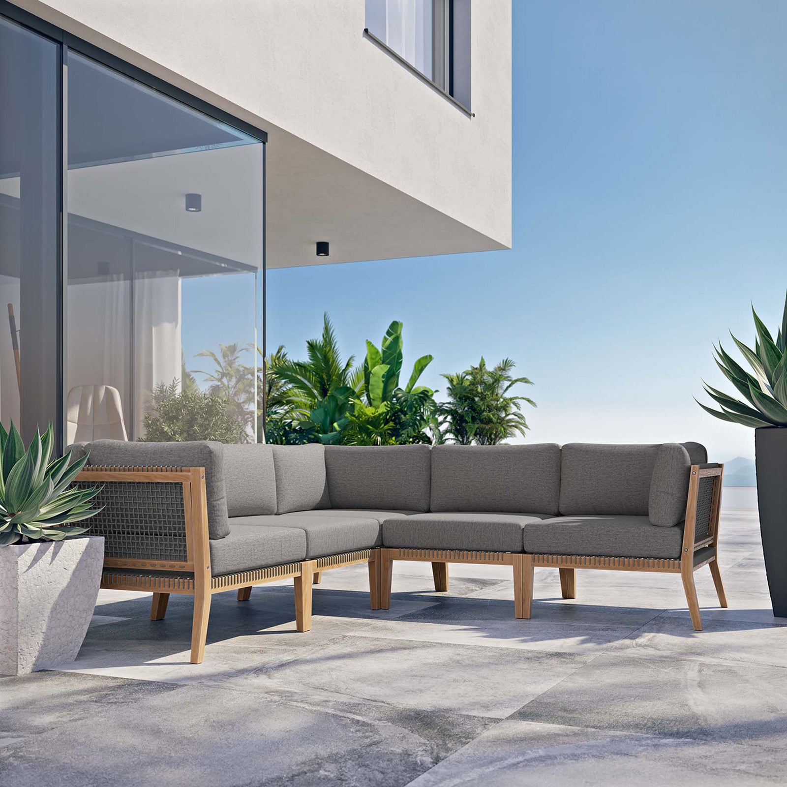 Modern patio setting with gray graphite teak sectional positioned against a glass-walled contemporary home || EEI-6123-GRY-GPH || front_angle_room