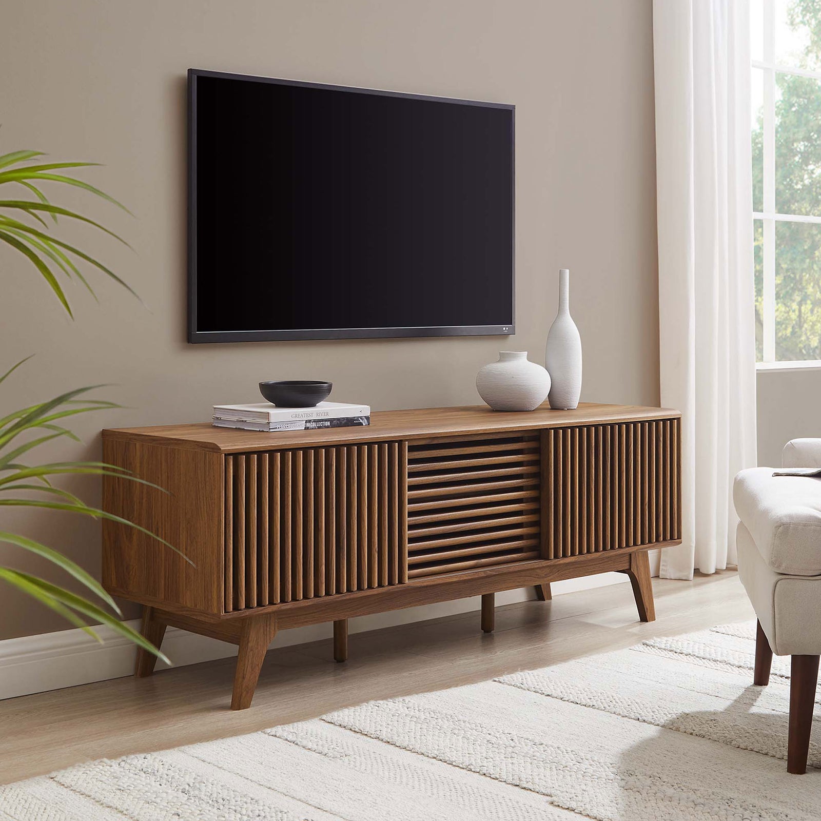 Walnut slatted-door TV stand anchors a bright living room beneath a wall-mounted TV with minimalist decor || EEI-6180-WAL || front_angle_room
