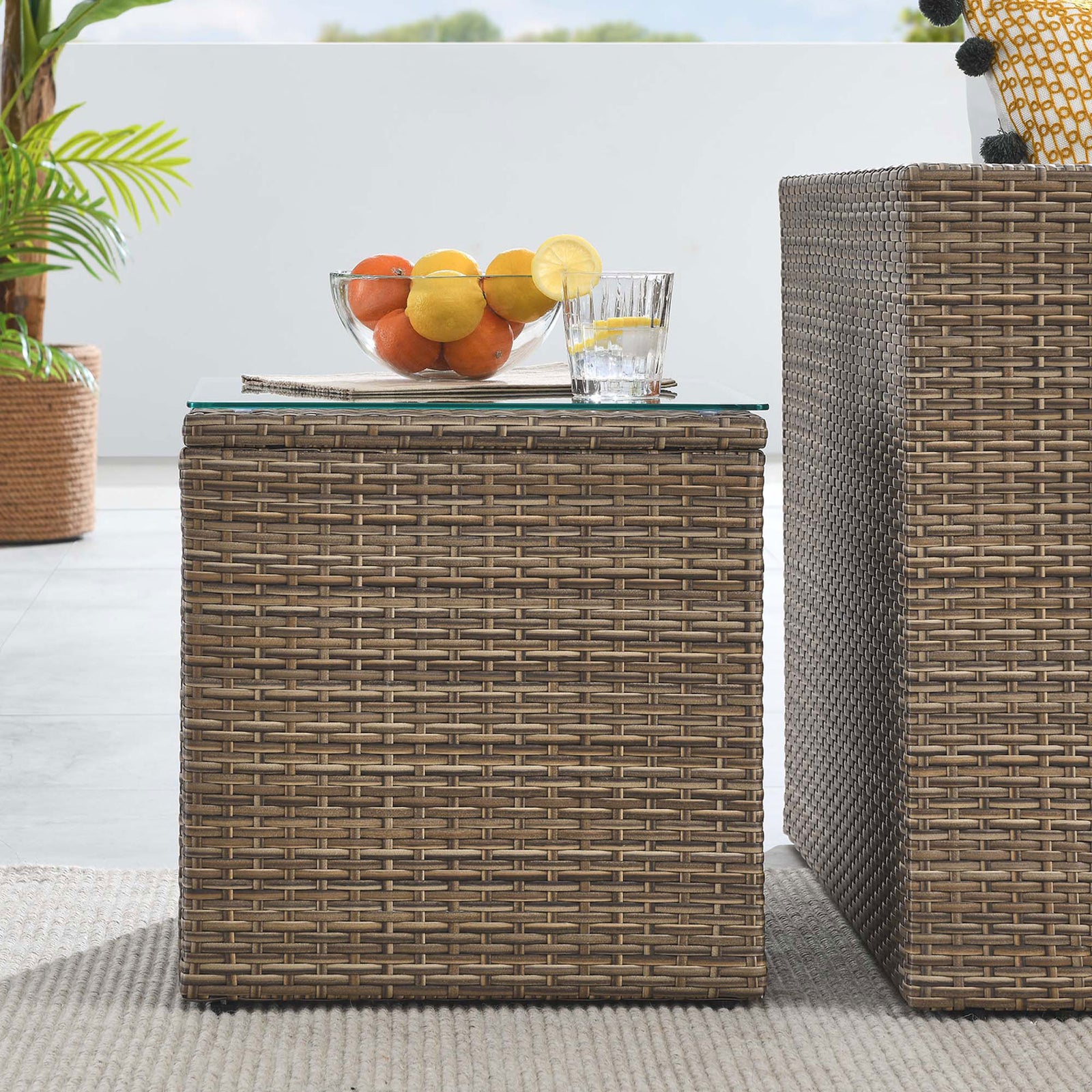 Brown rattan side table beside matching outdoor seating with glass top display surface || EEI-6240 || front_room