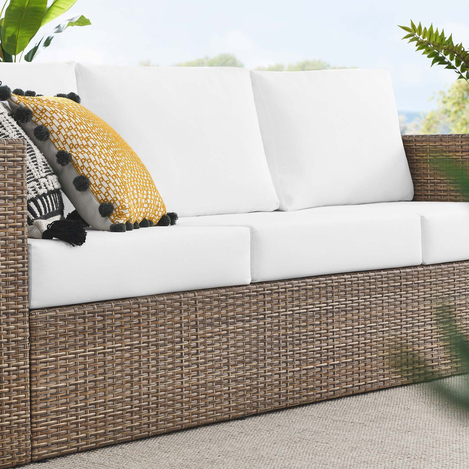 Convene outdoor sofa styled with pillows, showing textured wicker base and crisp white cushions on the patio. || EEI-6245-CAP-WHI || detail_room
