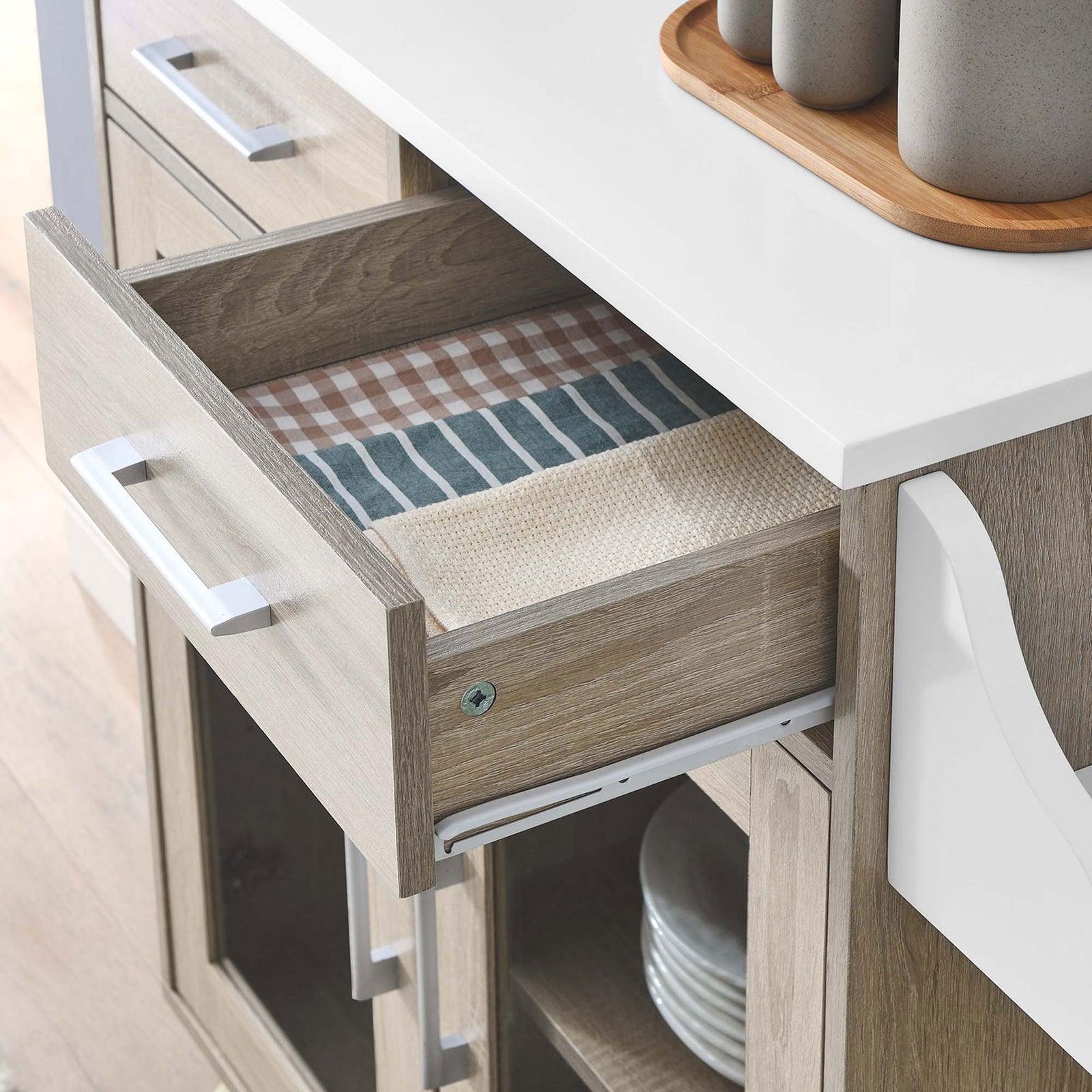 Open drawer of kitchen cart neatly storing linens beneath a smooth white work surface in a modern room || EEI-6276-OAK-WHI || storage_open_room