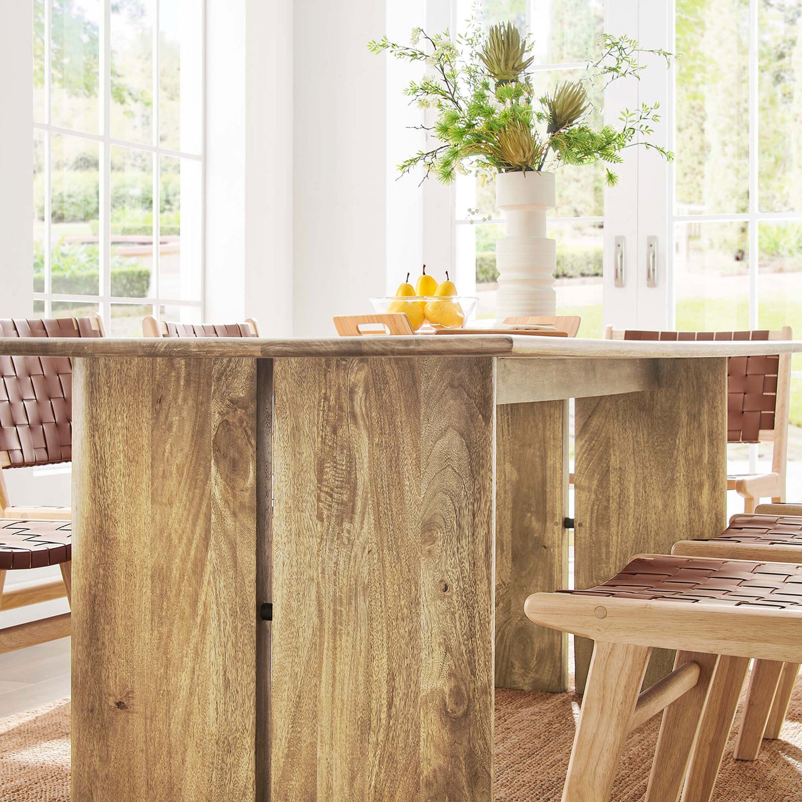 Room detail of the 86 inch oak dining table base paired with woven chairs and fresh greenery. || EEI-6340-OAK || detail_room