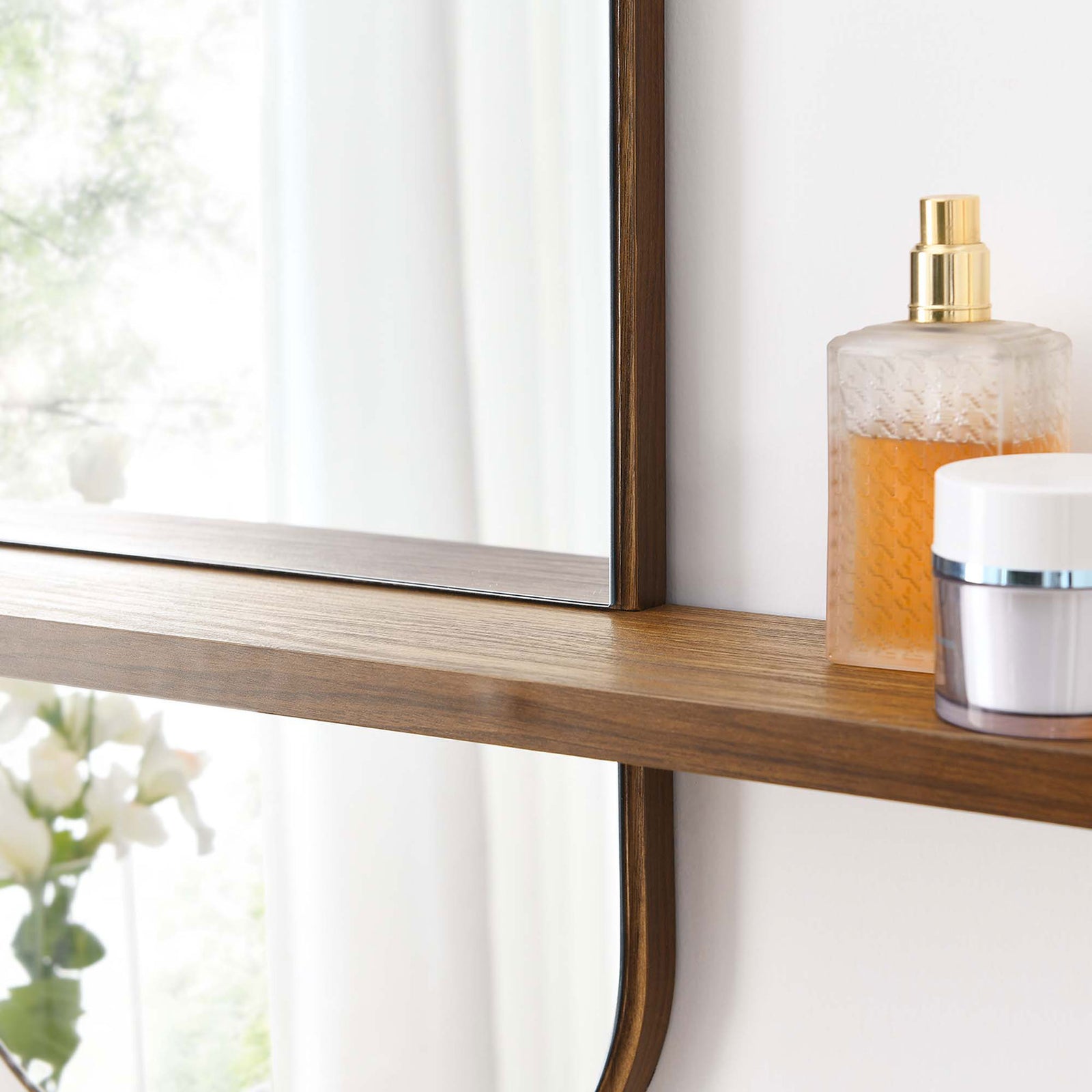 Walnut mirror shelf holding skincare essentials beside bright blooms and natural light. || EEI-6349-WAL || storage_room