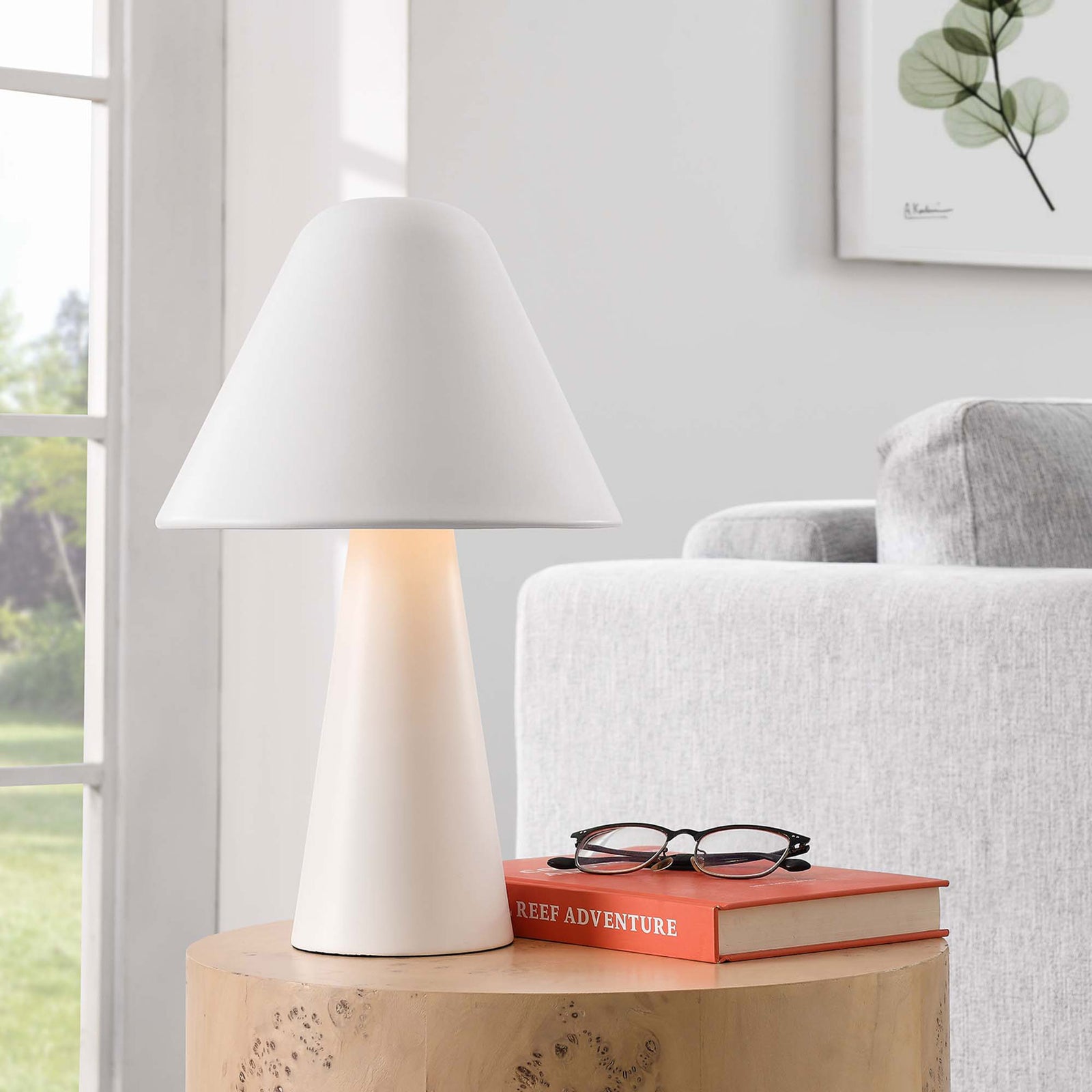 Illuminated white mushroom table lamp casts a soft, welcoming glow beside a modern sofa. || EEI-6529-WHI || front_angle_on_room