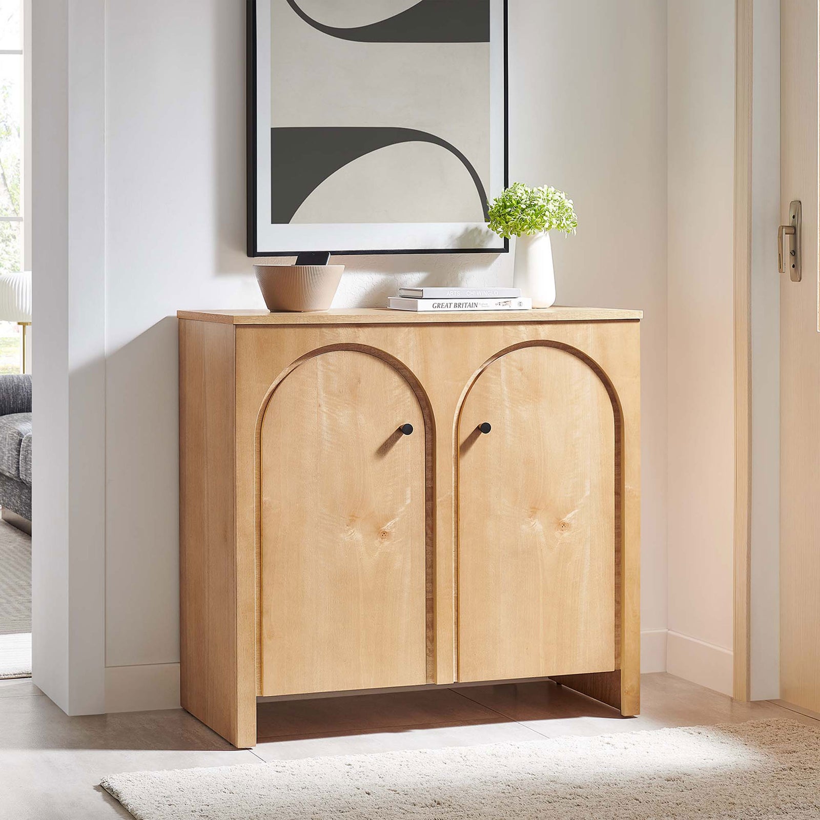 Oak arched-door cabinet warms a bright entryway styled with art, books, and greenery || EEI-6537-OAK || front_angle_room