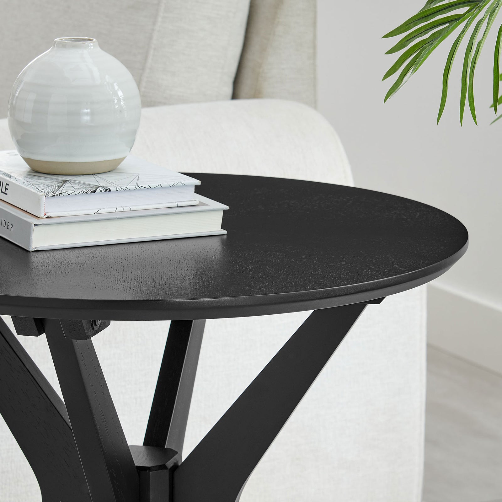 Round black side table styled with books and decor beside a sofa, ideal for modern lounge spaces || EEI-6558-BLK || detail_room
