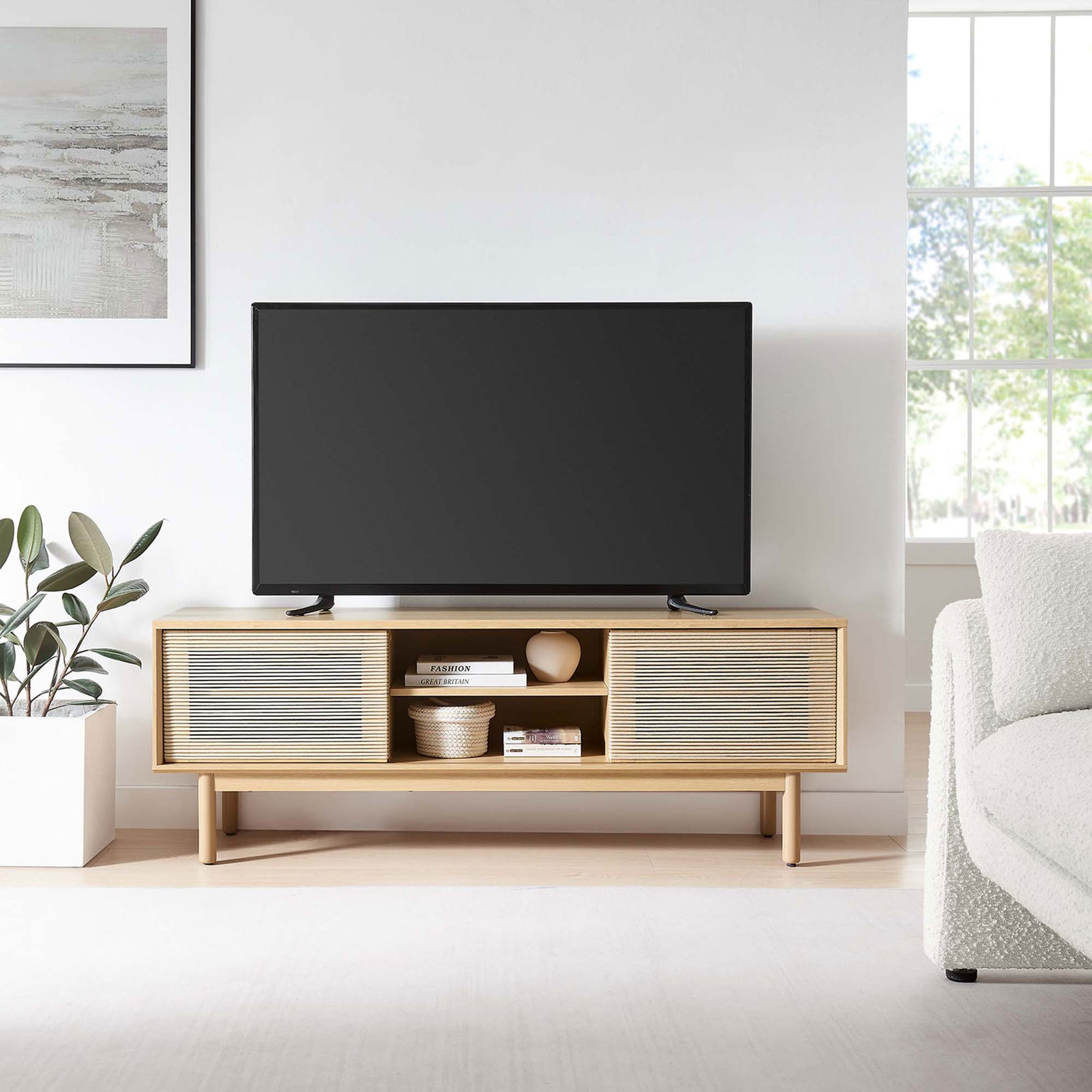 Milo 59 inch oak tan TV stand supporting a flat screen TV, styled with decor in a bright modern living room || EEI-6584-OAK-TAN || front_open_room