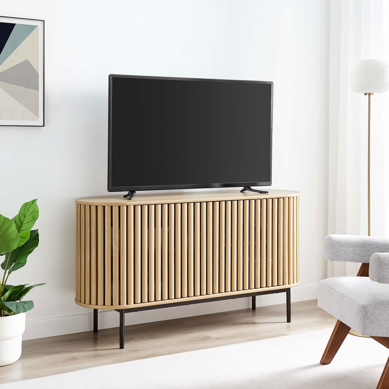 Fortitude oak sideboard used as a TV console in a bright living room with modern seating and greenery. || EEI-6590-OAK || front_angle_room