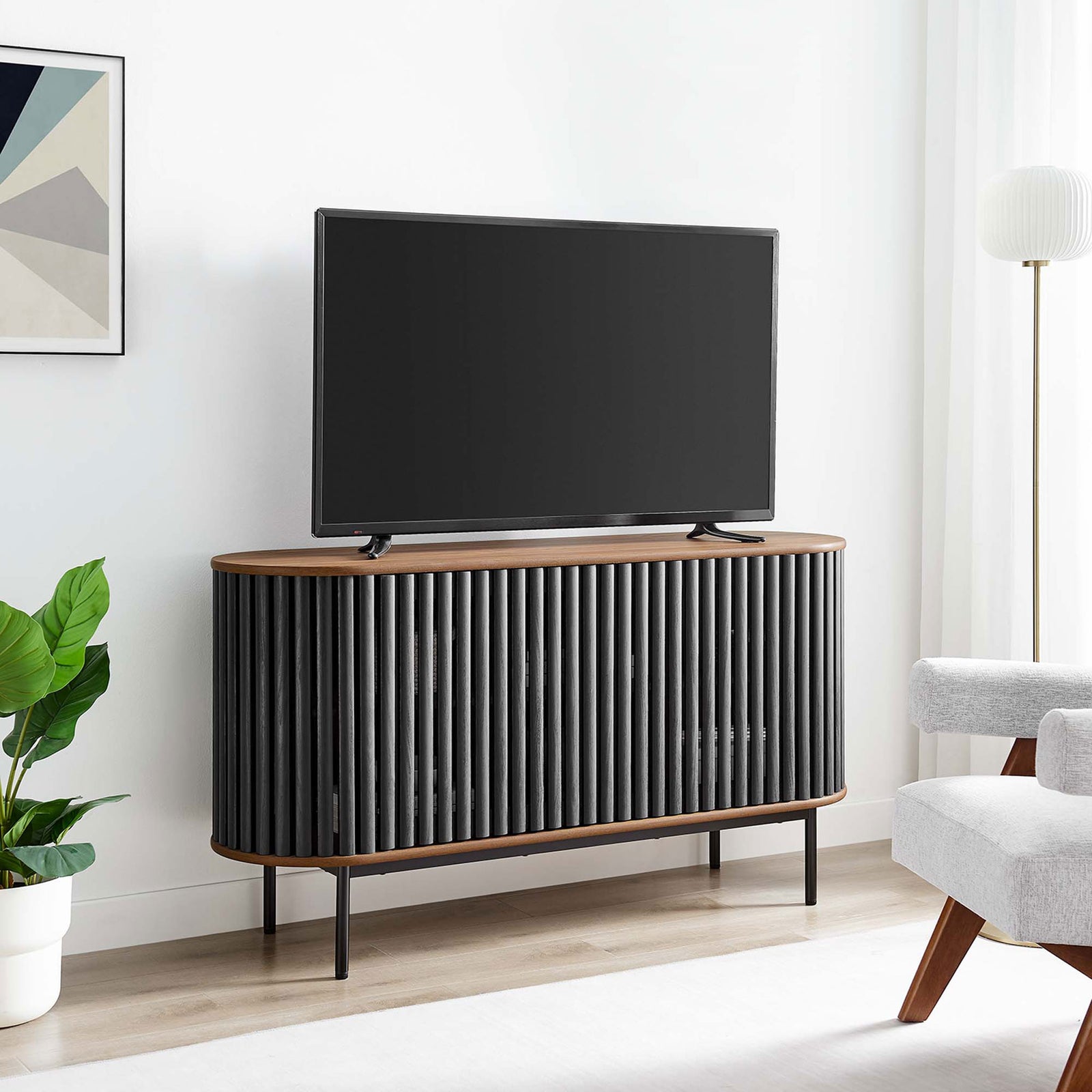Oval sideboard used as a media console in a bright living room, supporting a large flat-screen TV. || EEI-6590-WAL-BLK || front_room