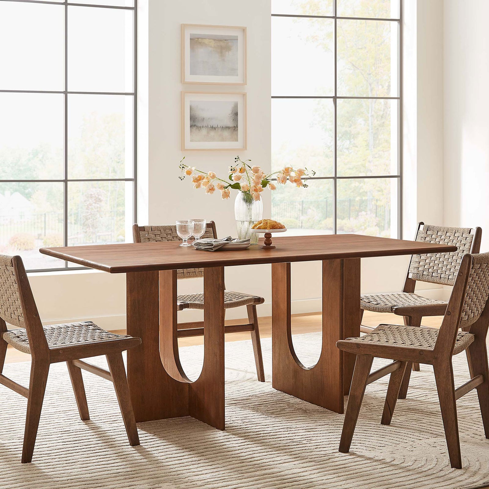 Rivian dining table anchoring a modern space, pairing its sculptural walnut base with coordinating woven chairs || EEI-6593-WAL || front_angle_room