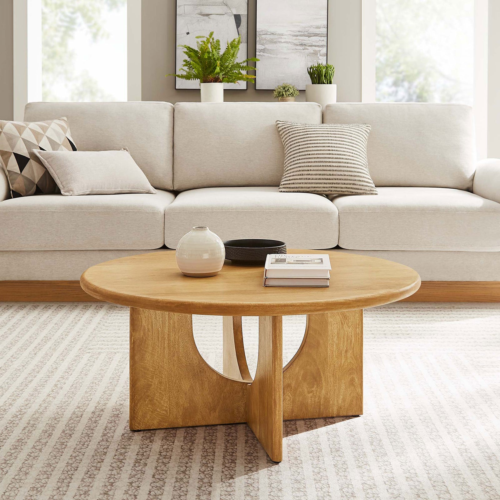 Modern round coffee table anchors the living room with its sculptural oak pedestal and smooth top. || EEI-6594-OAK || front_angle_room