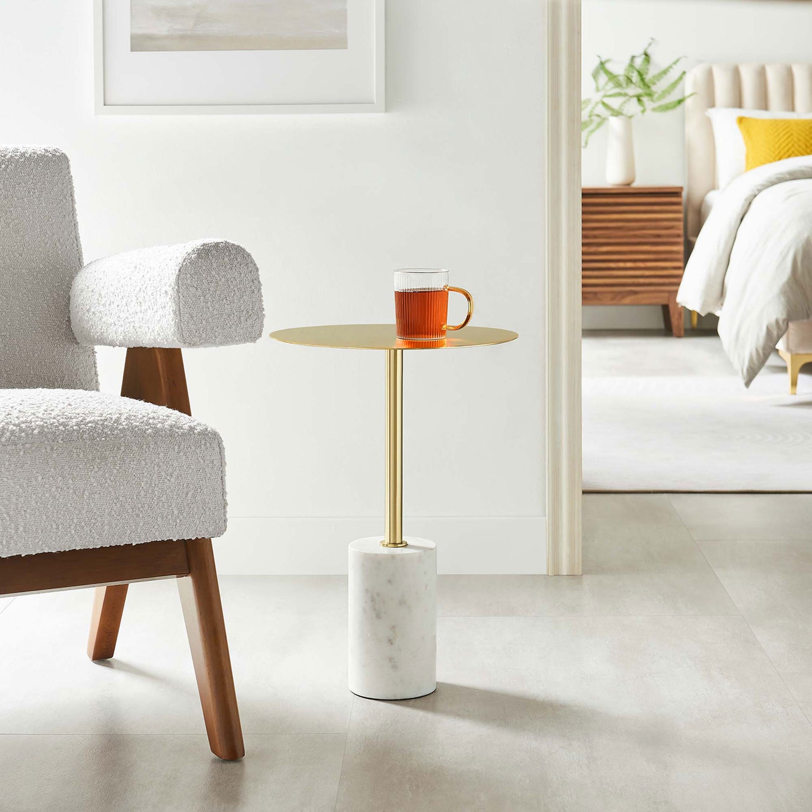 Slim brass and marble side table next to an accent chair, bringing modern elegance to a bright bedroom || EEI-6605-WHI-BRA || front_angle_room