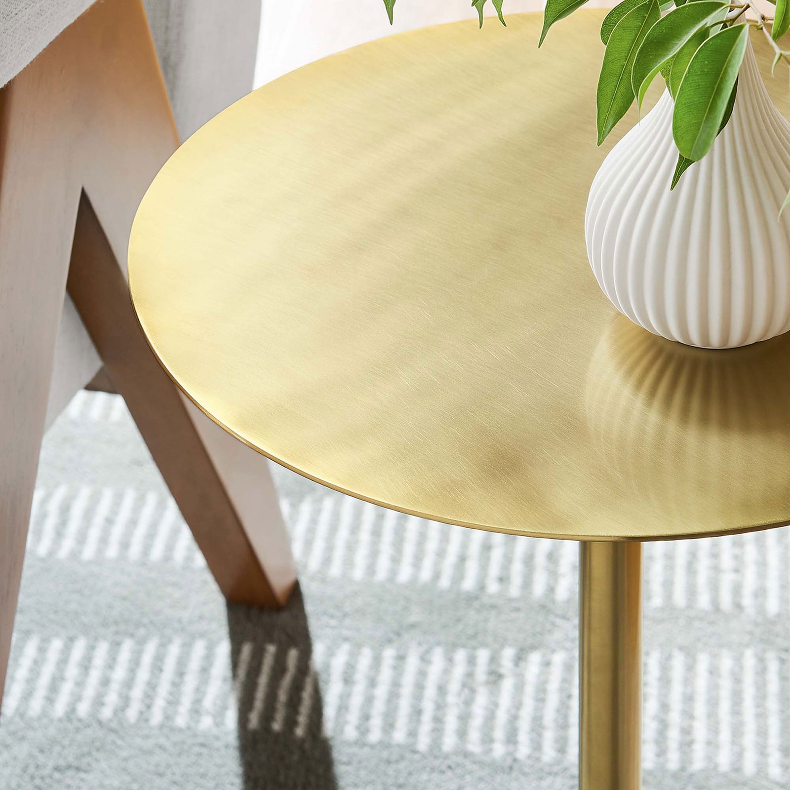 Brass tabletop adds a warm gleam beside a chair, styled with a sculpted vase and greenery || EEI-6606-WHI-BRA || detail_room