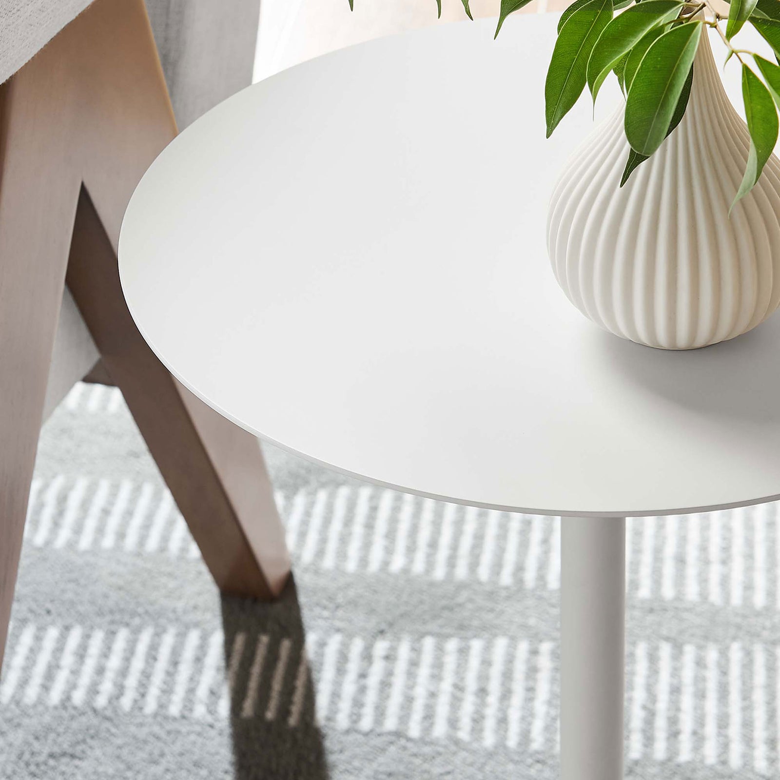 White round side table styled with a ribbed ceramic vase beside a sofa in a bright living room || EEI-6606-WHI-WHI || detail_room