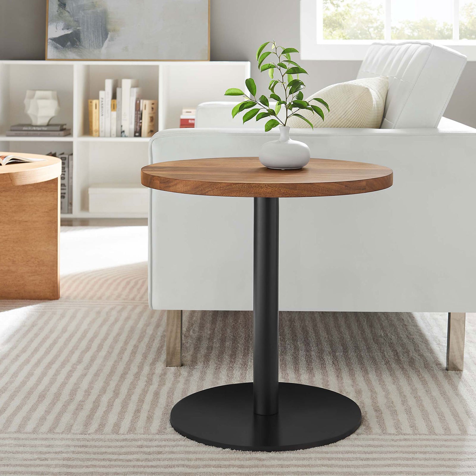 Viva round acacia side table with black pedestal base next to white armchair in bright lounge || EEI-6610-BLK-LOC || front_angle_room