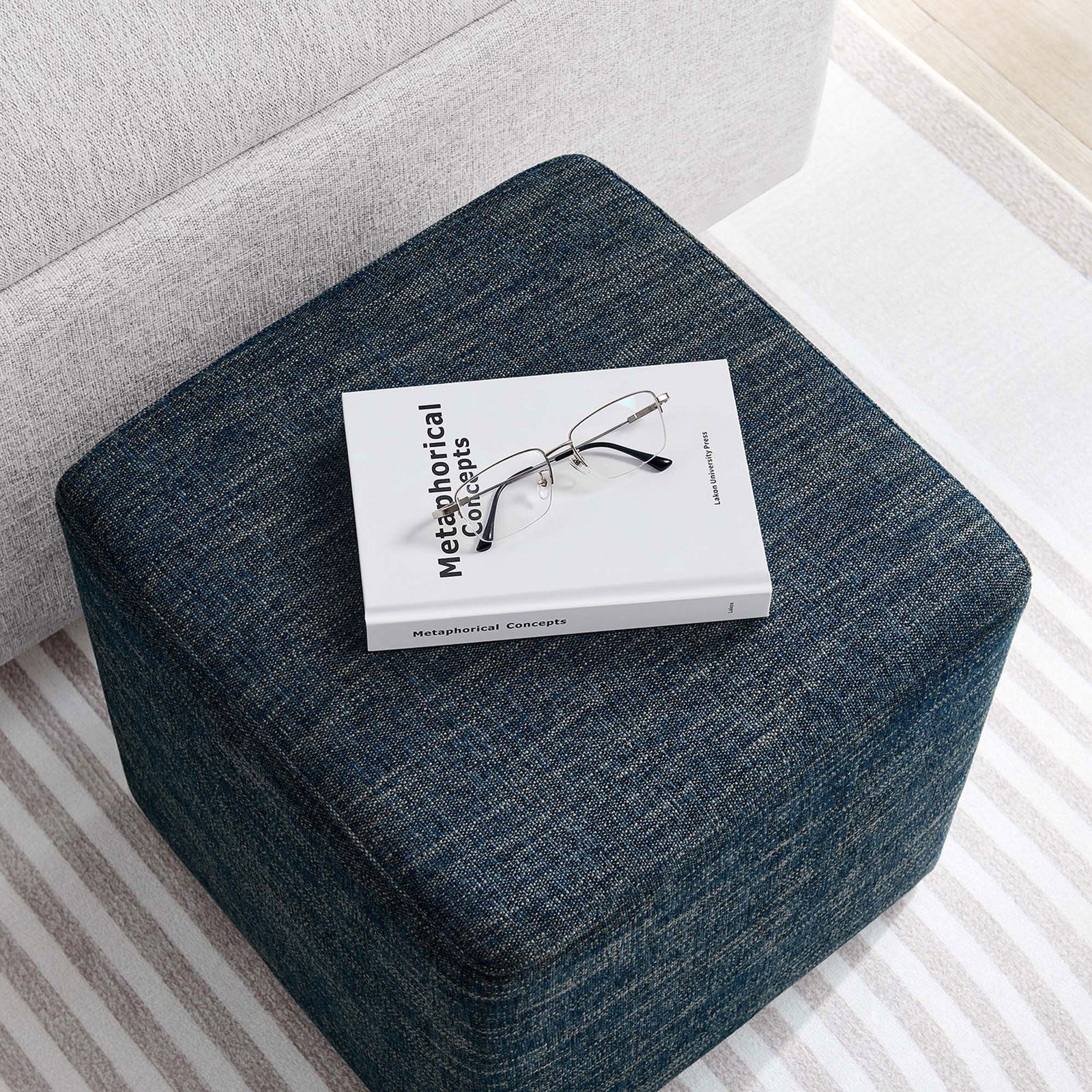 Ottoman used as a convenient tabletop, styled with a book and glasses beside a modern sofa || EEI-6636-HEA || top_angle_room