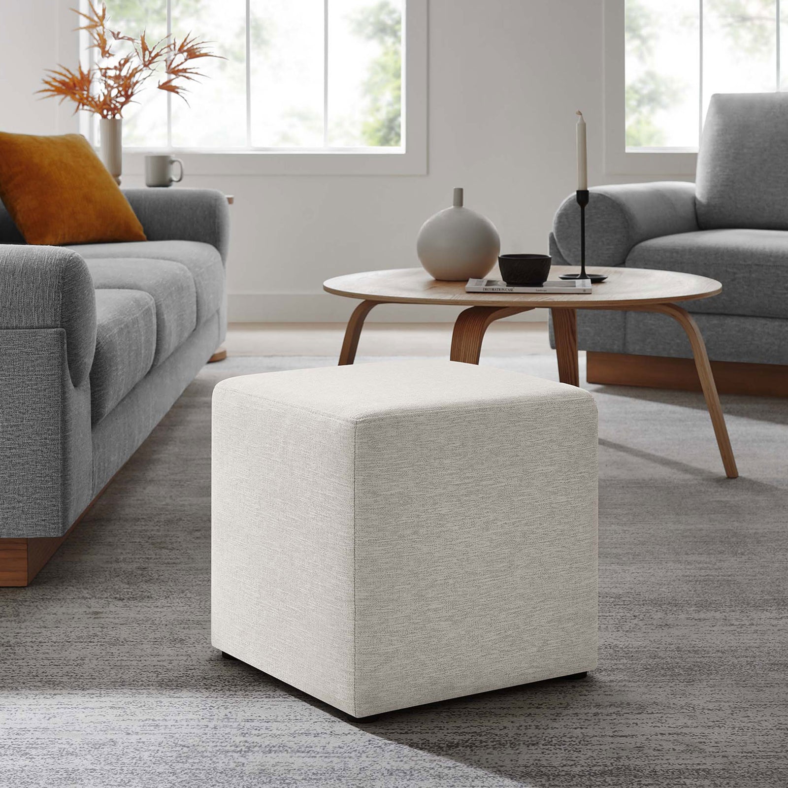 Heathered ivory ottoman centered in a contemporary living room, offering flexible seating or a stylish perch. || EEI-6636-HEI || front_angle_room