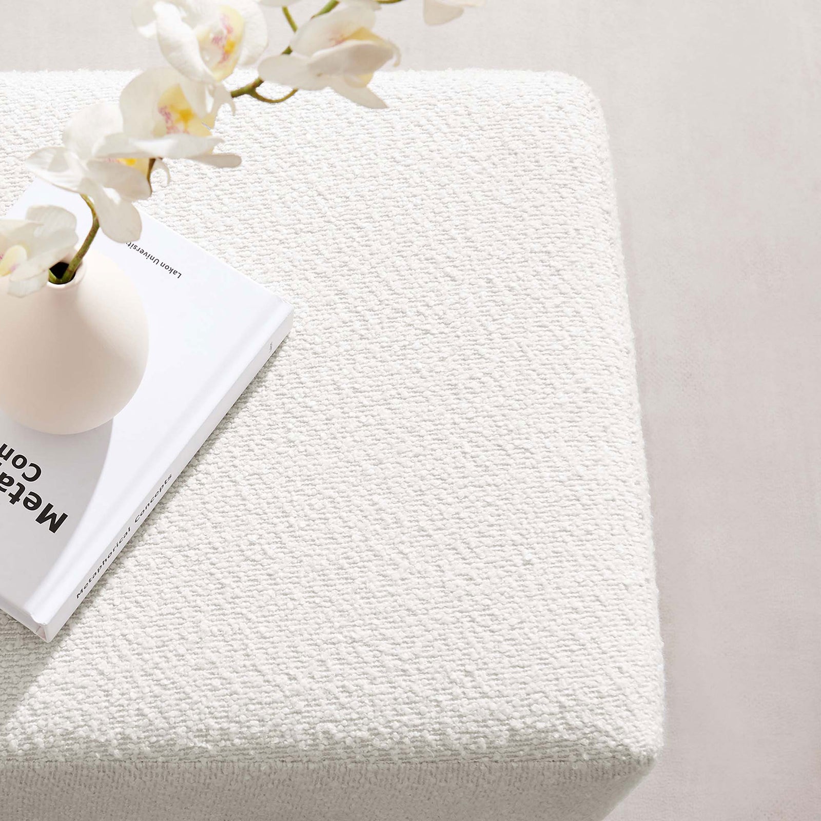 White boucle ottoman styled with a vase and book, creating a soft textured surface for decor or resting essentials. || EEI-6641-CLO-WAL || detail_room