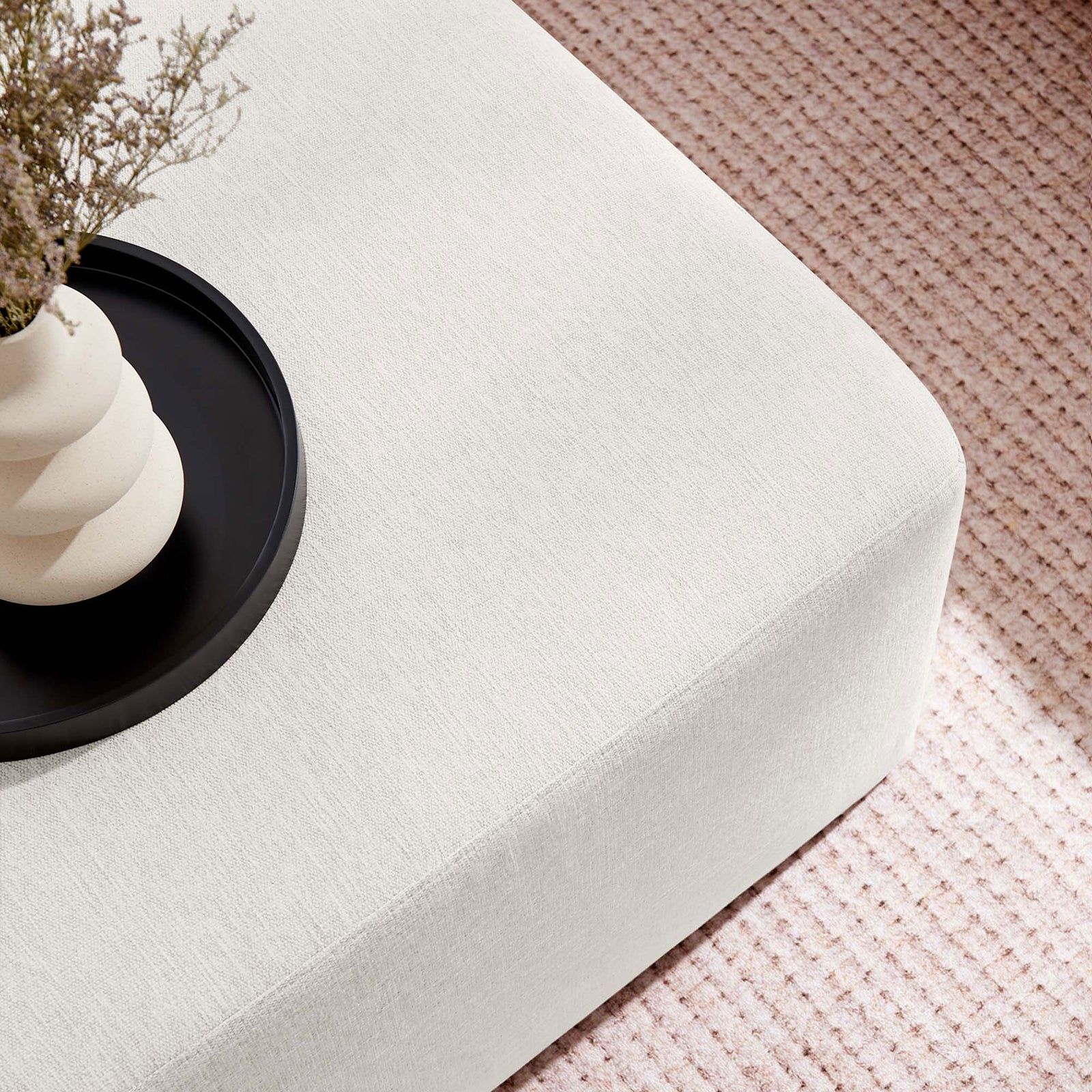 Ivory ottoman styled as a coffee table with a modern tray and vase over a textured neutral rug || EEI-6642-HEI || detail_room