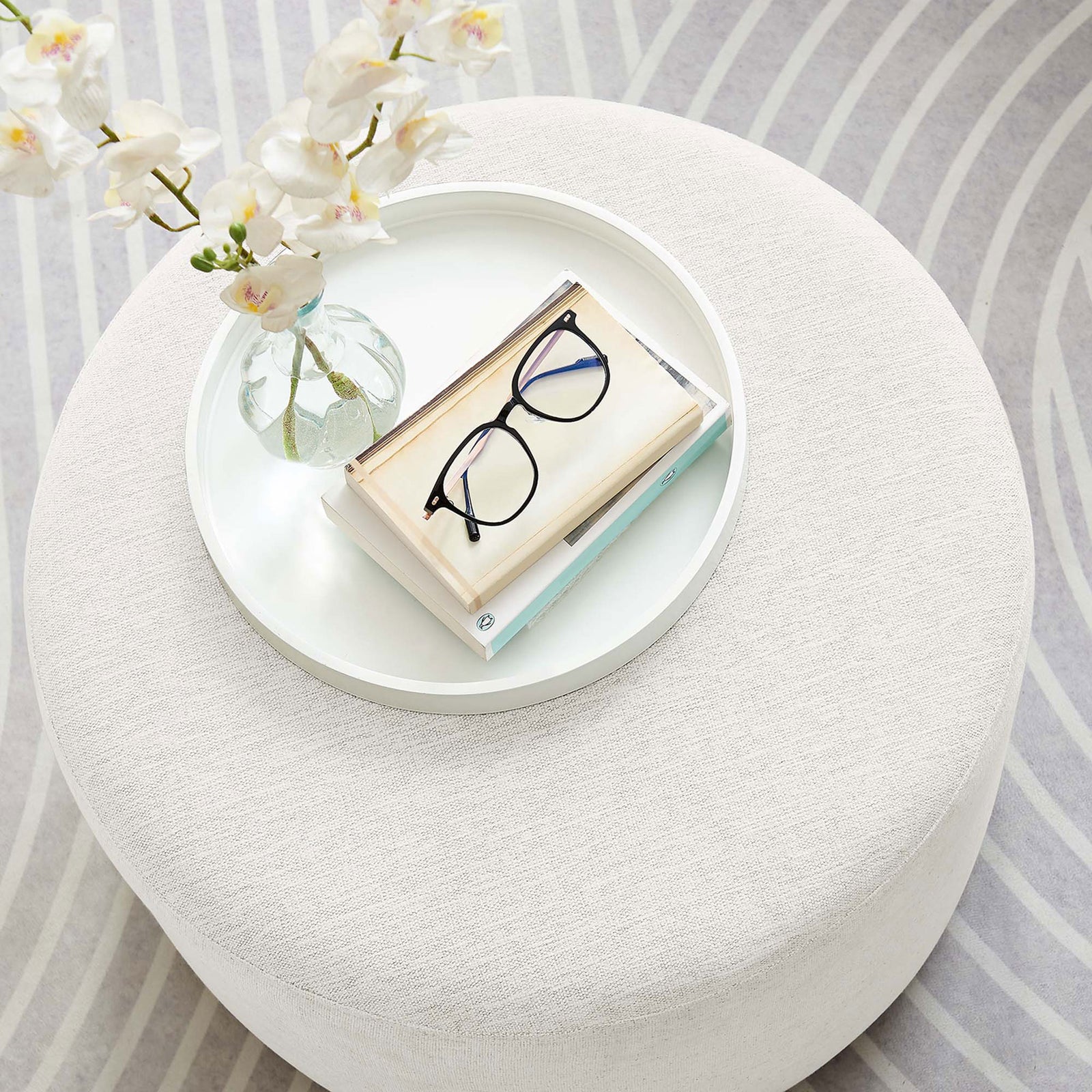Ivory round ottoman styled with a tray, flowers, and glasses on a patterned area rug || EEI-6645-HEI || detail_room