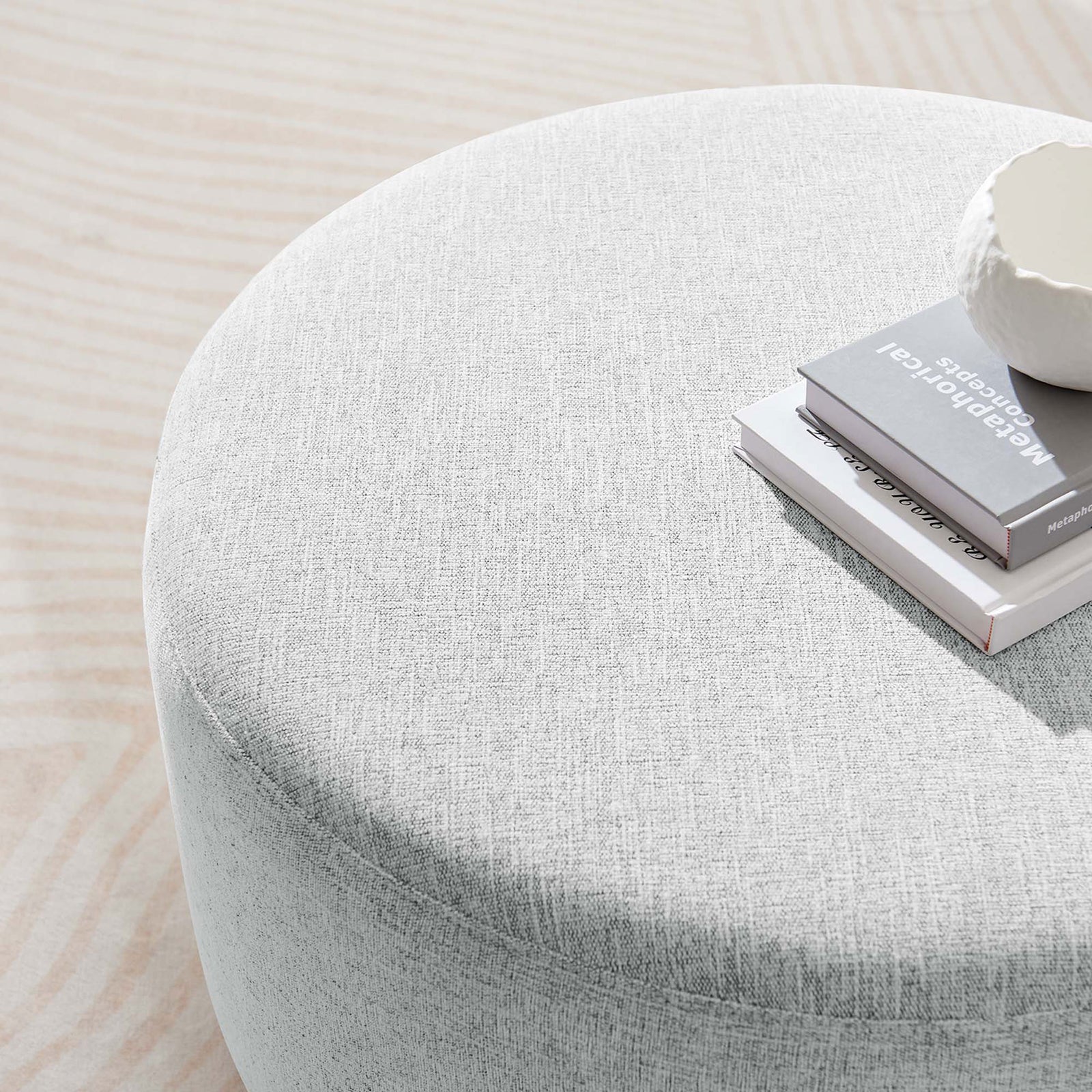 Heathered light gray round ottoman styled as a coffee table with books and decor in a bright room || EEI-6647-HLG || top_room