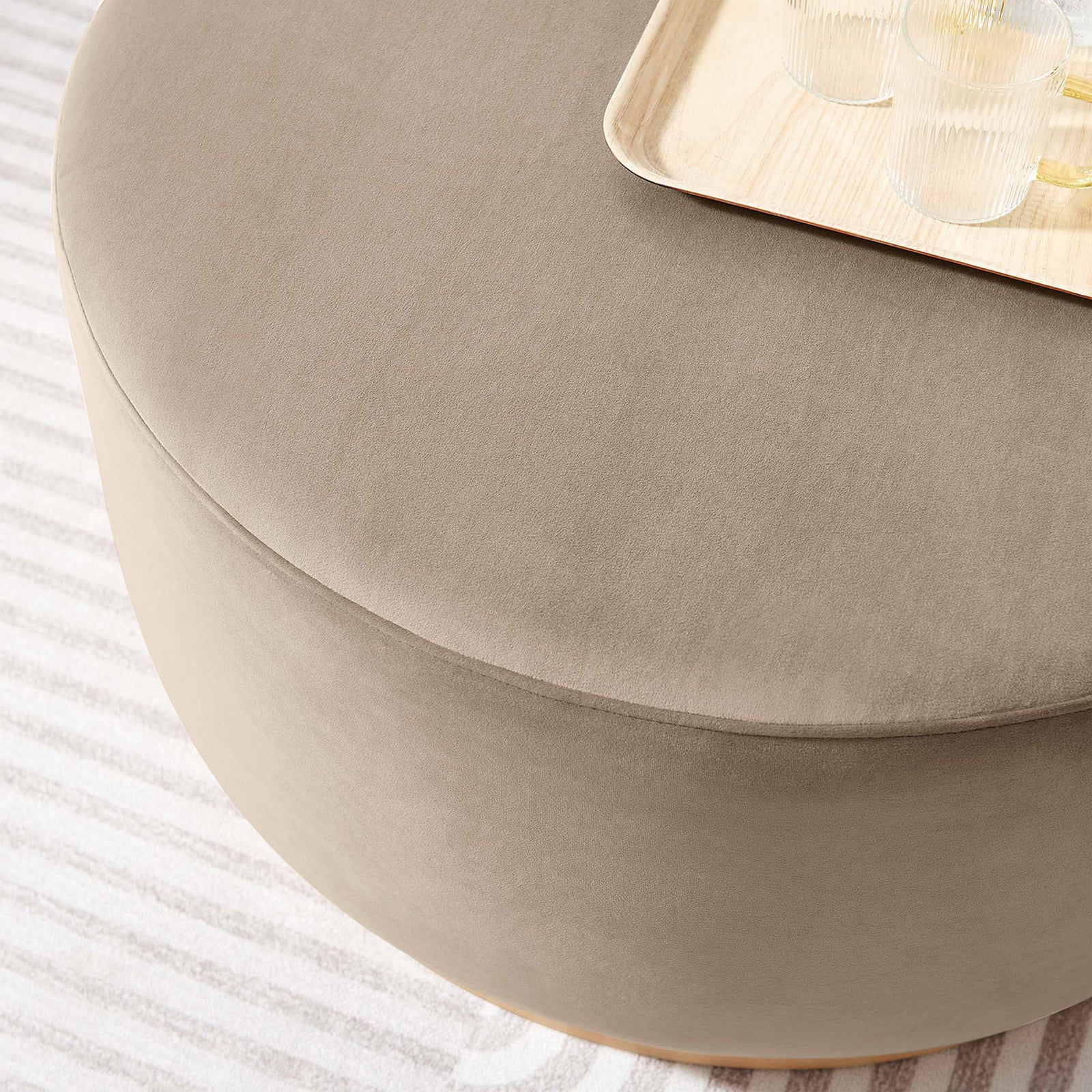 Taupe round ottoman styled as a coffee table with tray and glassware on a striped rug || EEI-6648-TAU-NAT || detail_room