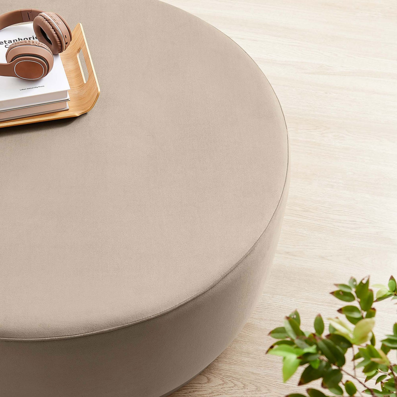 Large taupe round ottoman topped with tray, headphones, and decor on a light wood floor || EEI-6650-TAU-NAT || detail_room