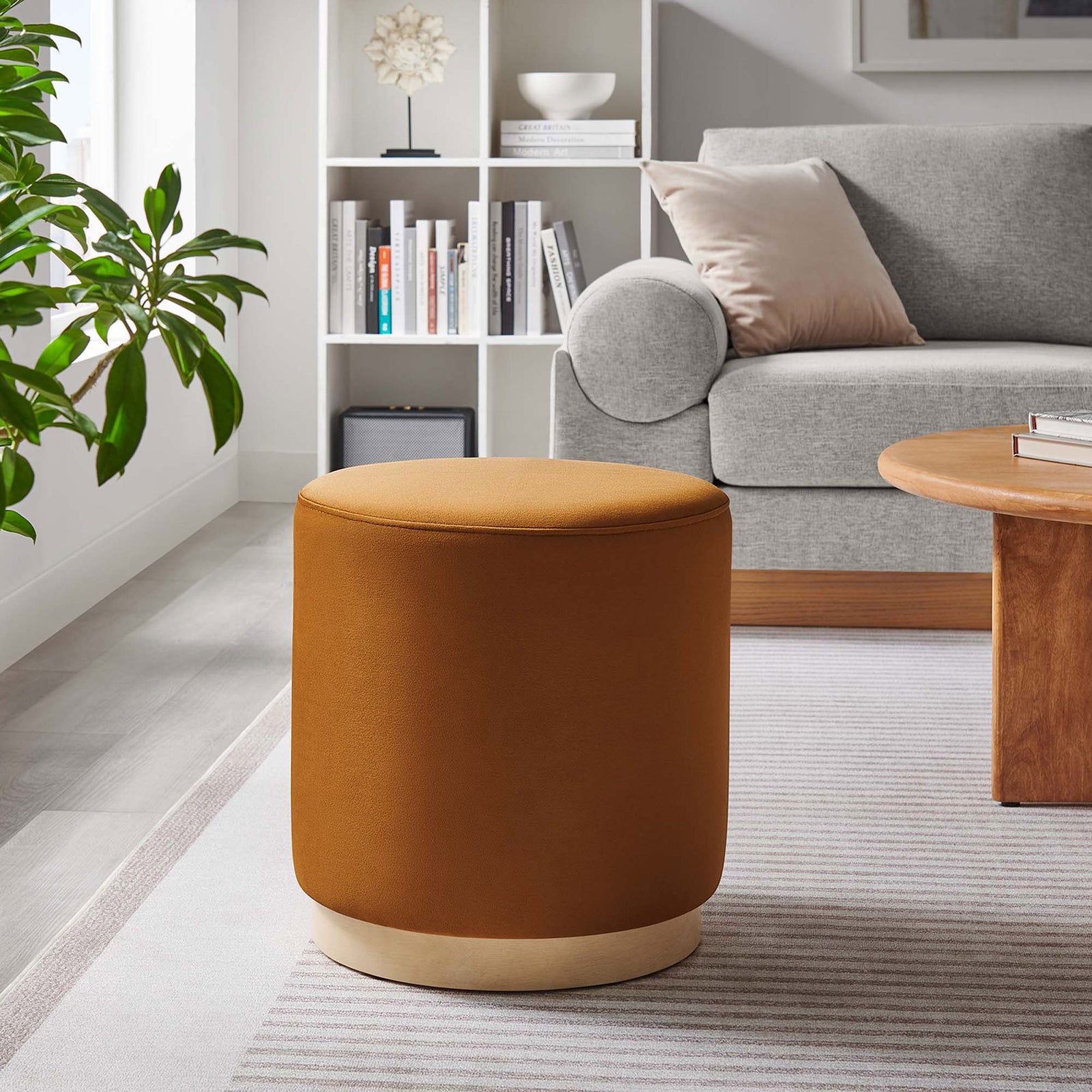 Elegant rust velvet ottoman anchors the seating area, pairing its soft curves with a pale wood base and rug || EEI-6652-RUS-NAT || front_angle_room