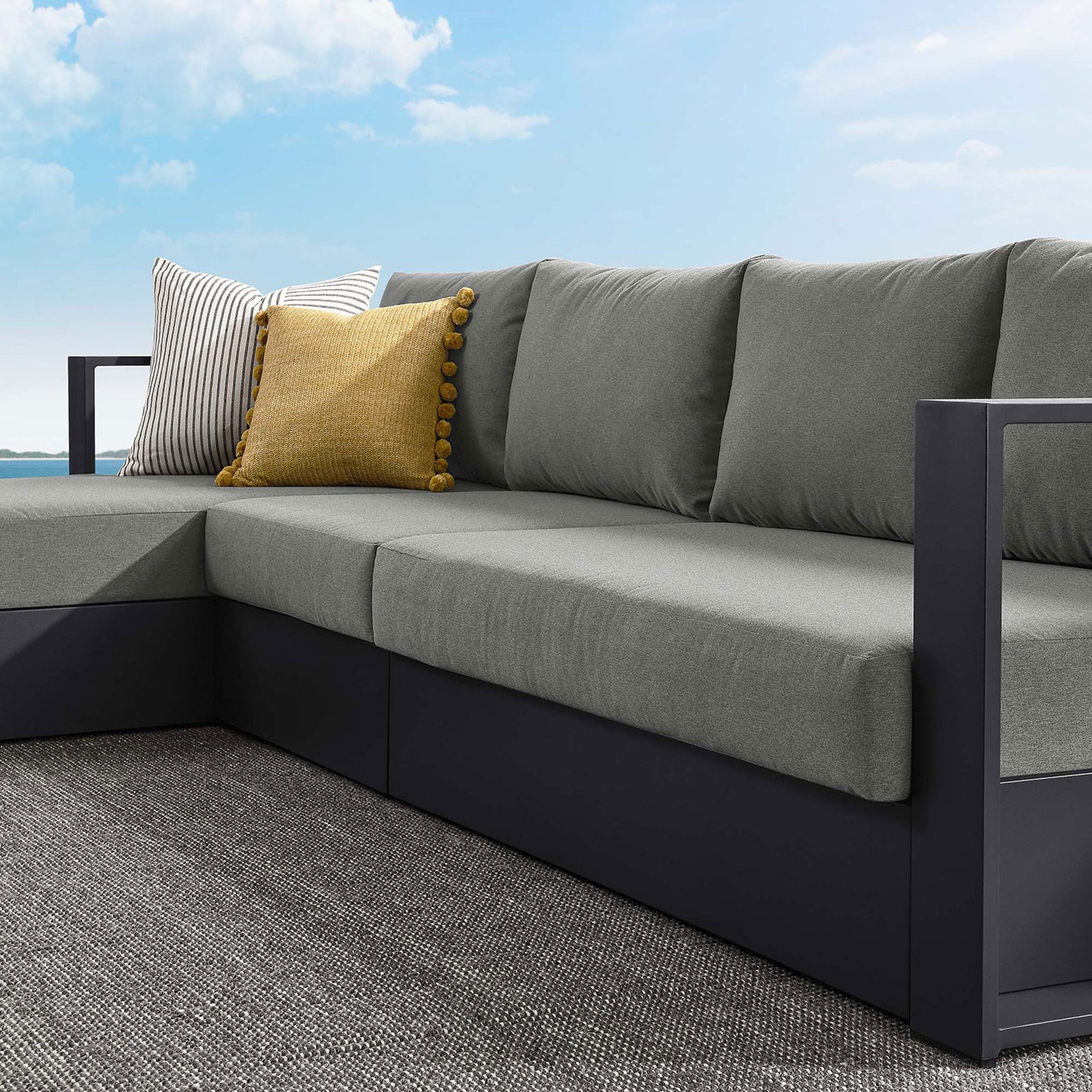 Charcoal cushions and angular armrest framed by striped and mustard outdoor throw pillows on a patio || EEI-6672-GRY-CHA || detail_room