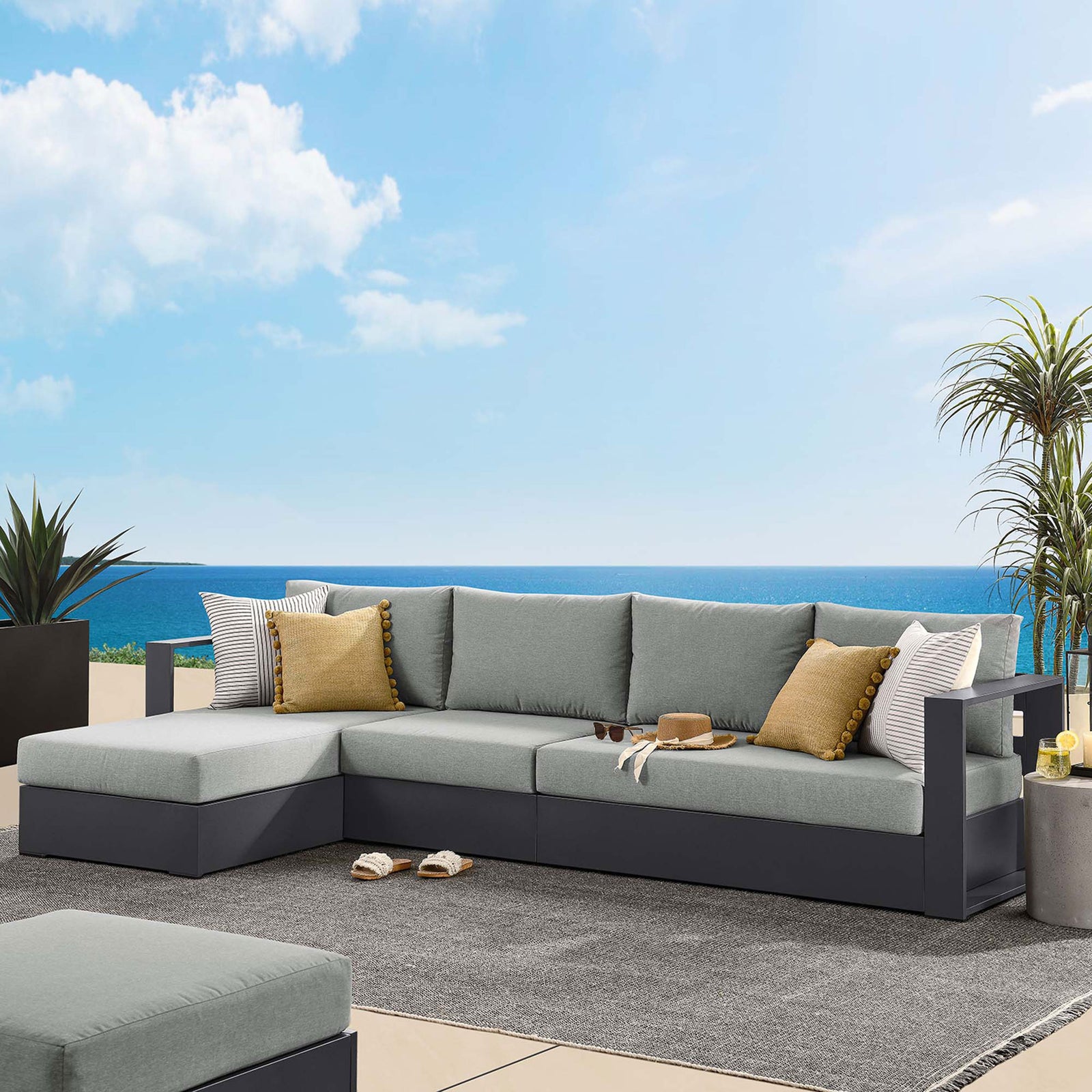 Left chaise sectional on a terrace overlooking the sea, styled with yellow pillows and coastal accents || EEI-6672-GRY-GRY || front_angle_room