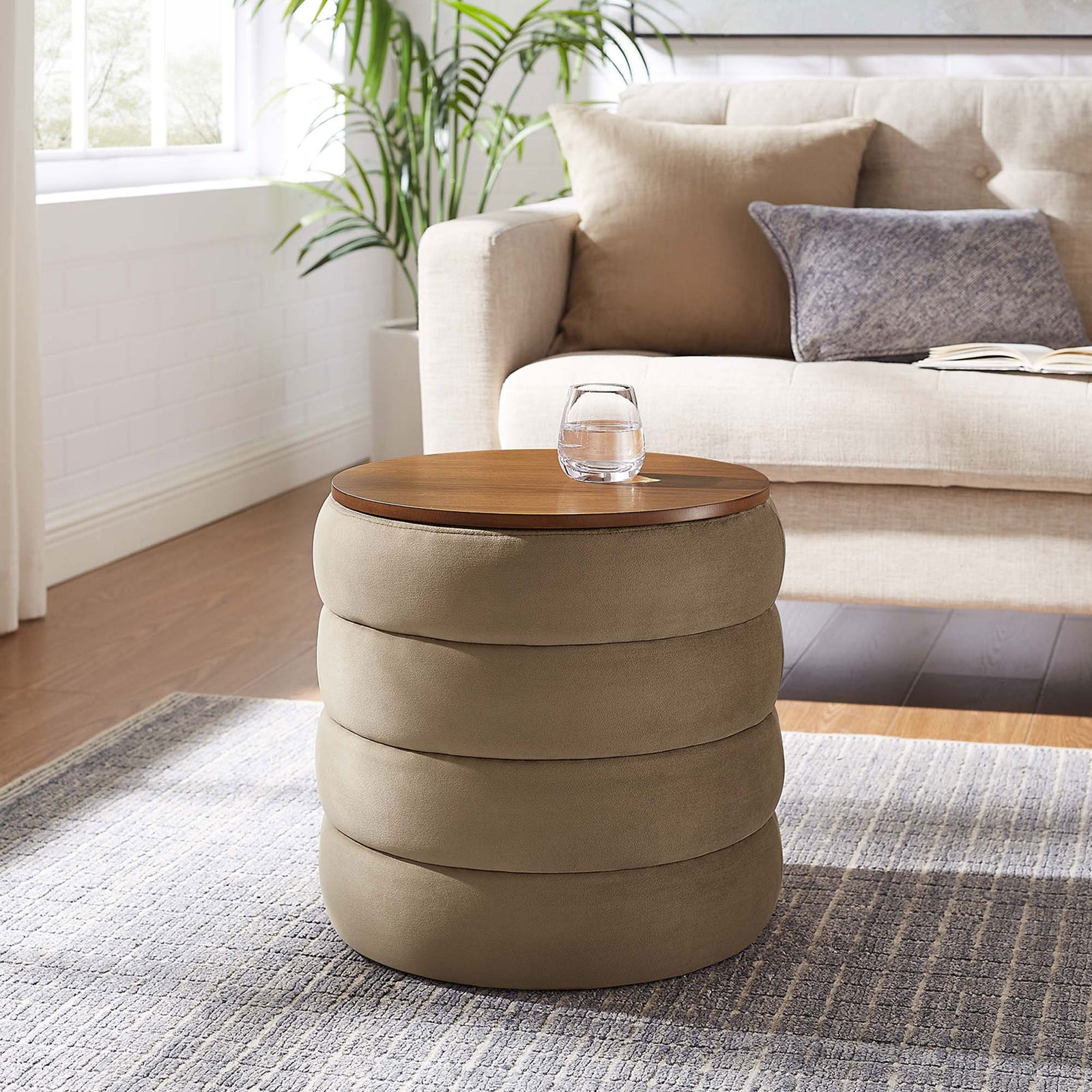 Round taupe velvet storage ottoman with wood top serving as side table in cozy living room || EEI-6684-TAU || front_angle_room