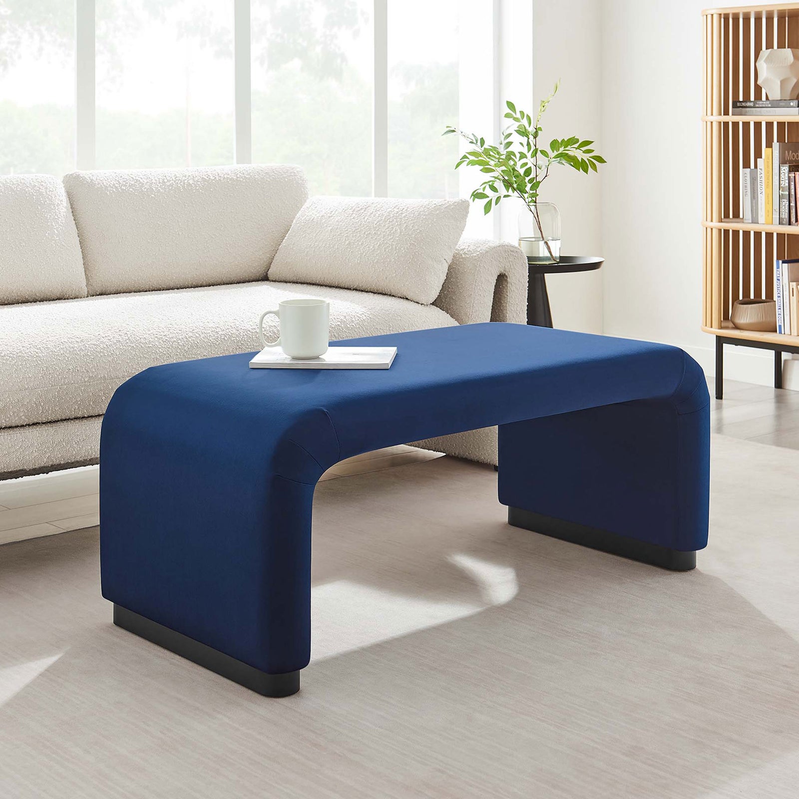 Velvet waterfall ottoman serving as a sleek coffee table in a bright minimalist living space || EEI-6735-BLK-MID || front_angle_room