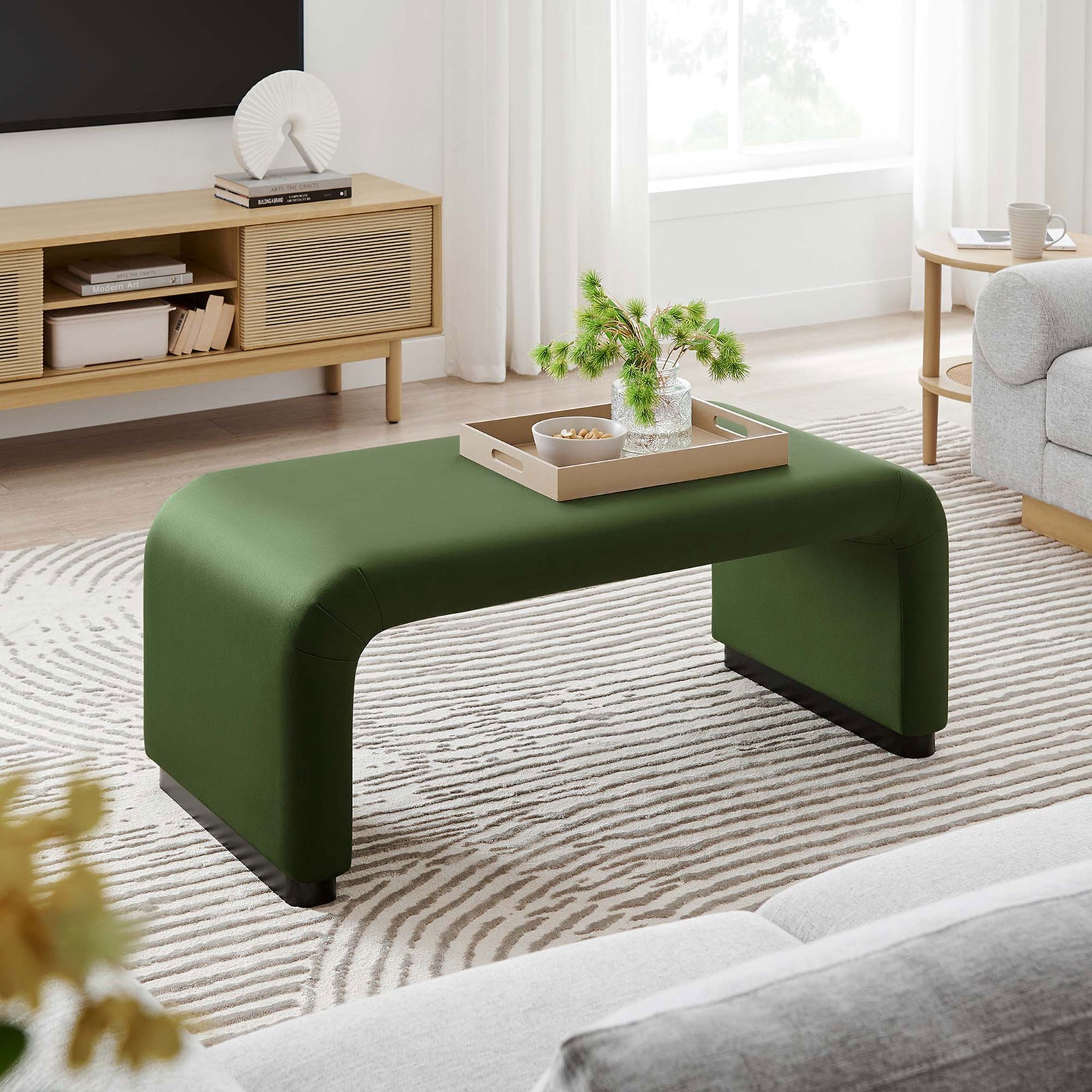 Black moss green velvet ottoman used as a low coffee table in a cozy living room with textured rug and sofa || EEI-6735-BLK-MOS || front_angle_room