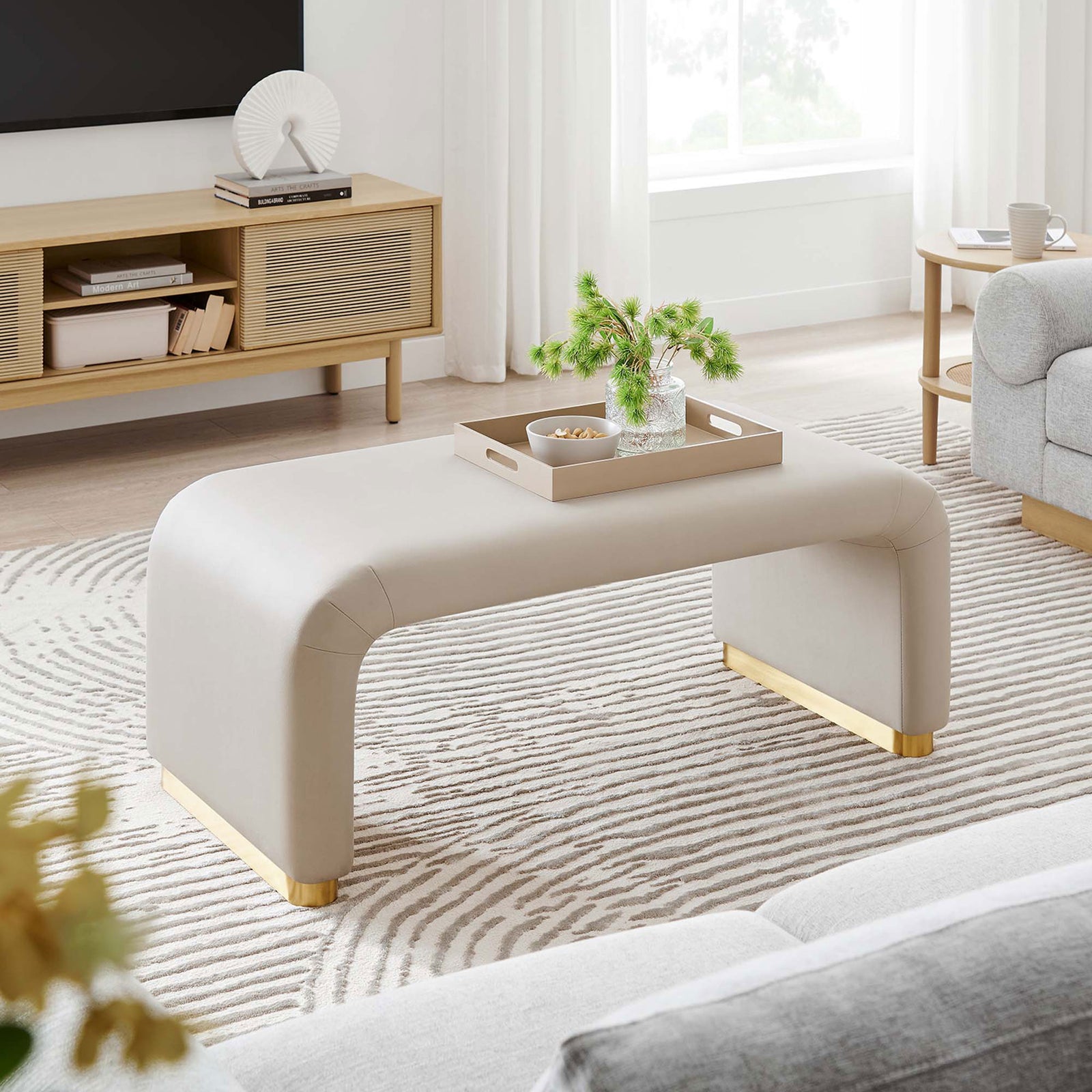 Modern room featuring the Koda waterfall ottoman in almond velvet paired with a striped rug and media console || EEI-6735-BRA-ALM || front_angle_room