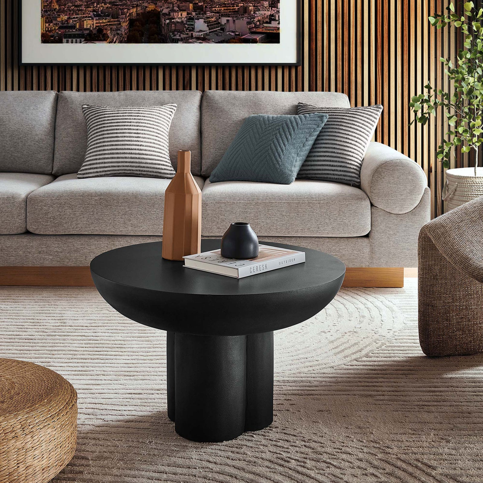 Striking round black coffee table elevates lounge spaces with sculptural pedestal form || EEI-6760-BLK || front_angle_room