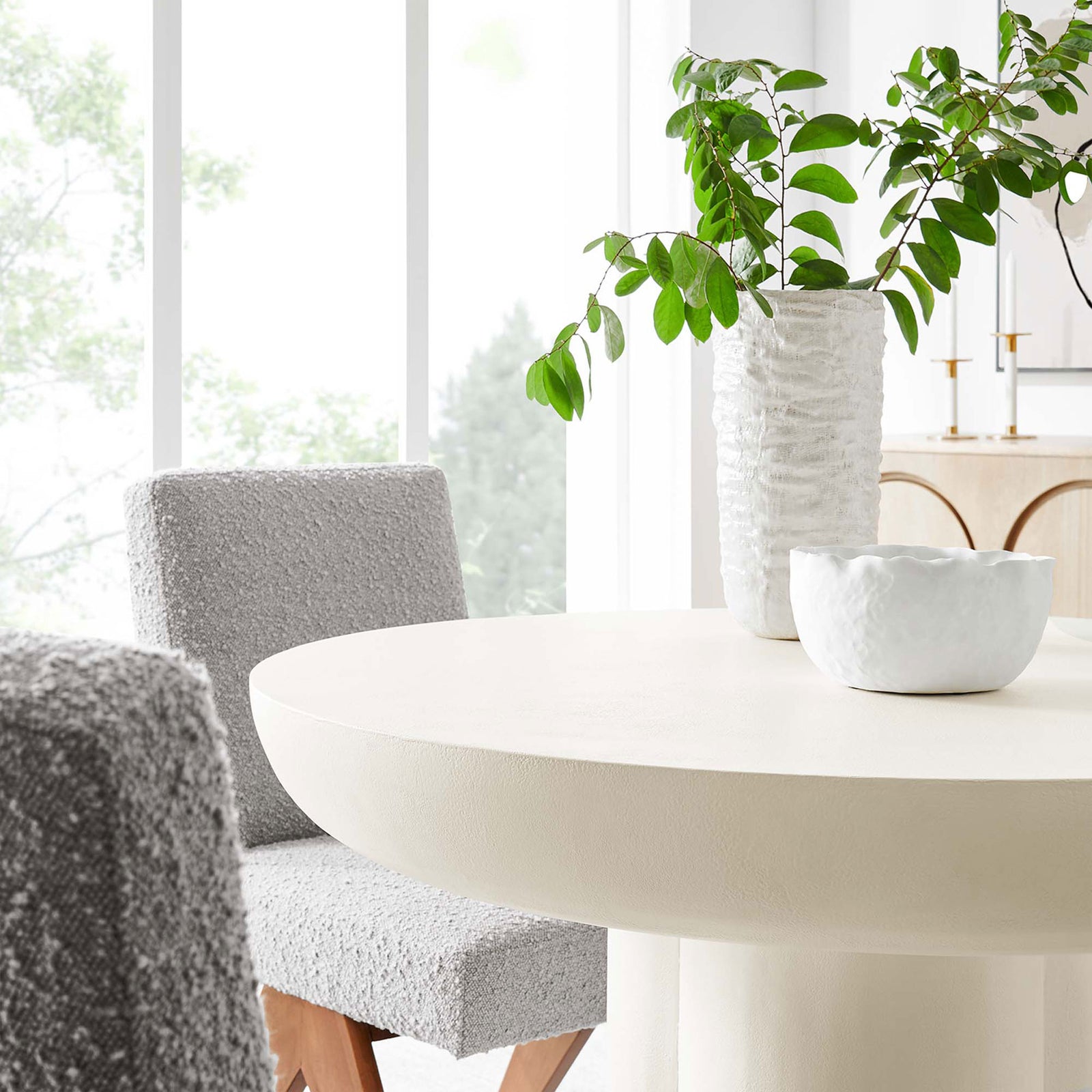 Caspian white round dining table styled in a bright dining room with cozy textured chairs and ceramic decor || EEI-6762-WHI || detail_room