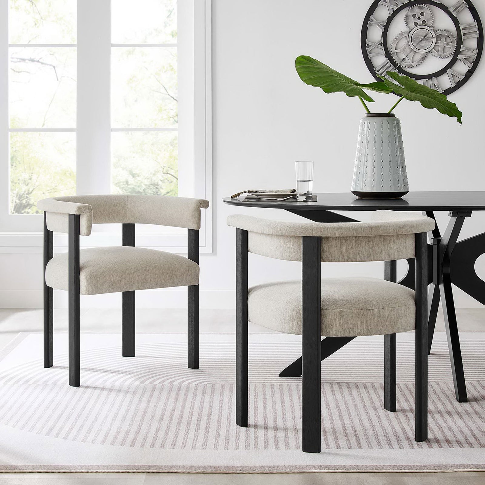 Pair of Imogen barrel dining chairs frame a sleek dining table in a bright contemporary room || EEI-6776-HEI-BLK || front_angle_multi_room