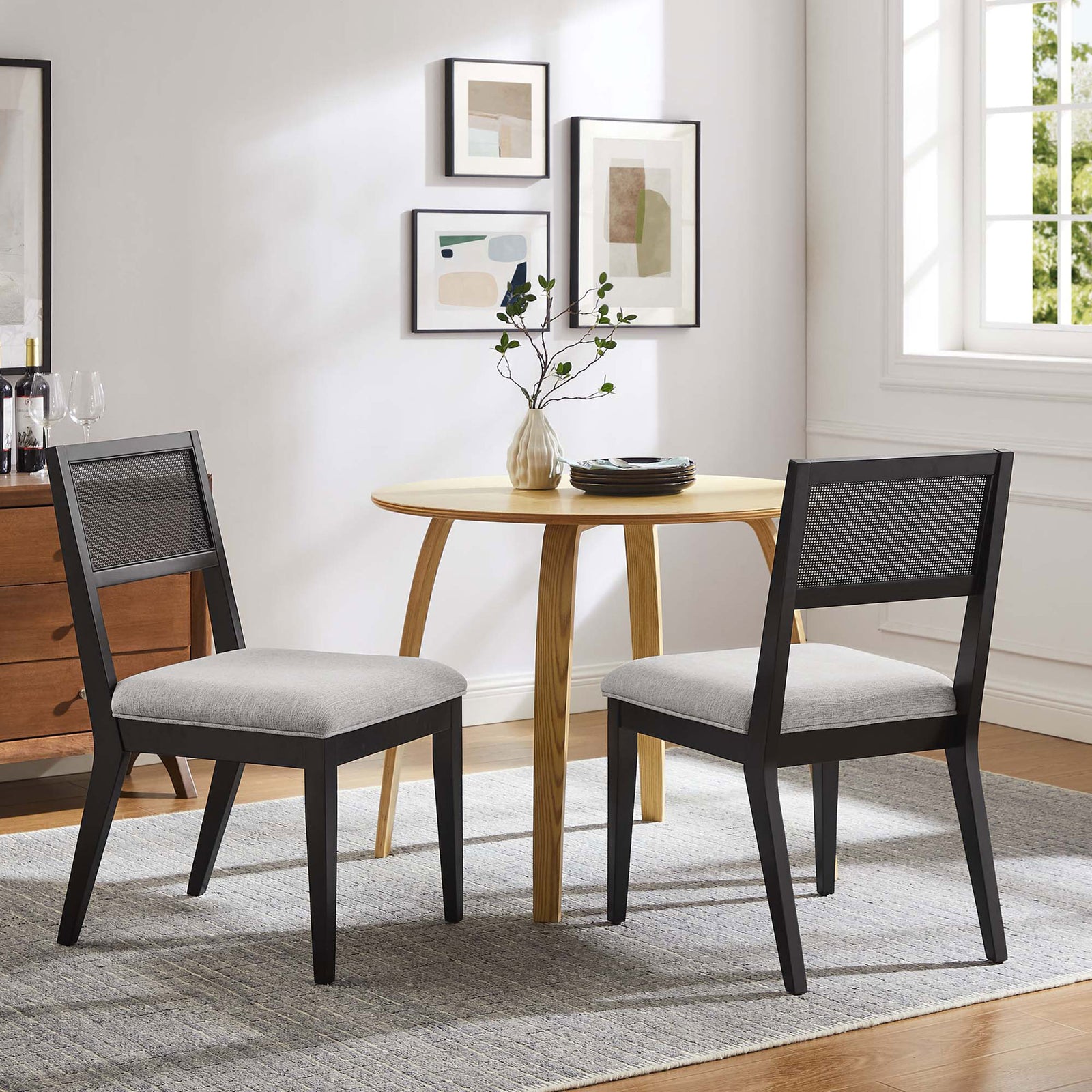Pair of faux rattan dining chairs frame a round wood table, creating a modern yet cozy dining nook || EEI-6781-BLK-HLG || front_angle_multi_room