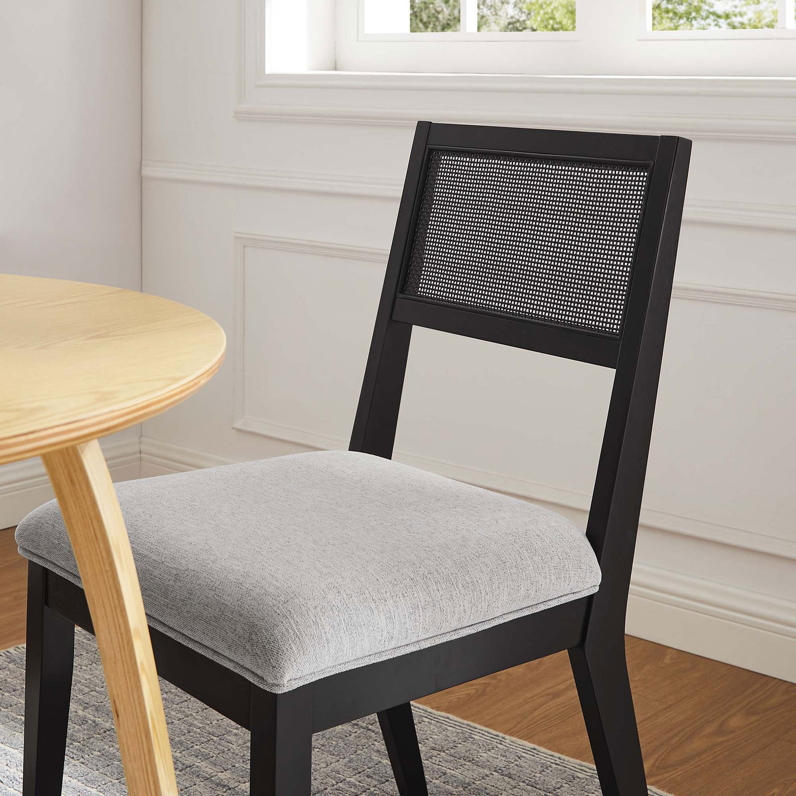 Light gray upholstered dining chair with cane back complements a warm wood table in a bright, inviting room || EEI-6781-BLK-HLG || detail_room