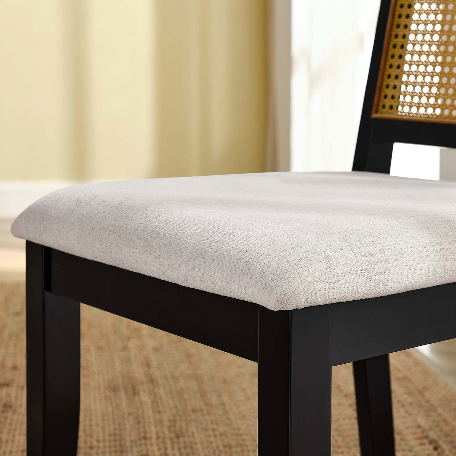 Ivory upholstered seat on black wood dining chair layered over a natural woven rug in a cozy room || EEI-6803-BLK-NAT-HEI || detail_room