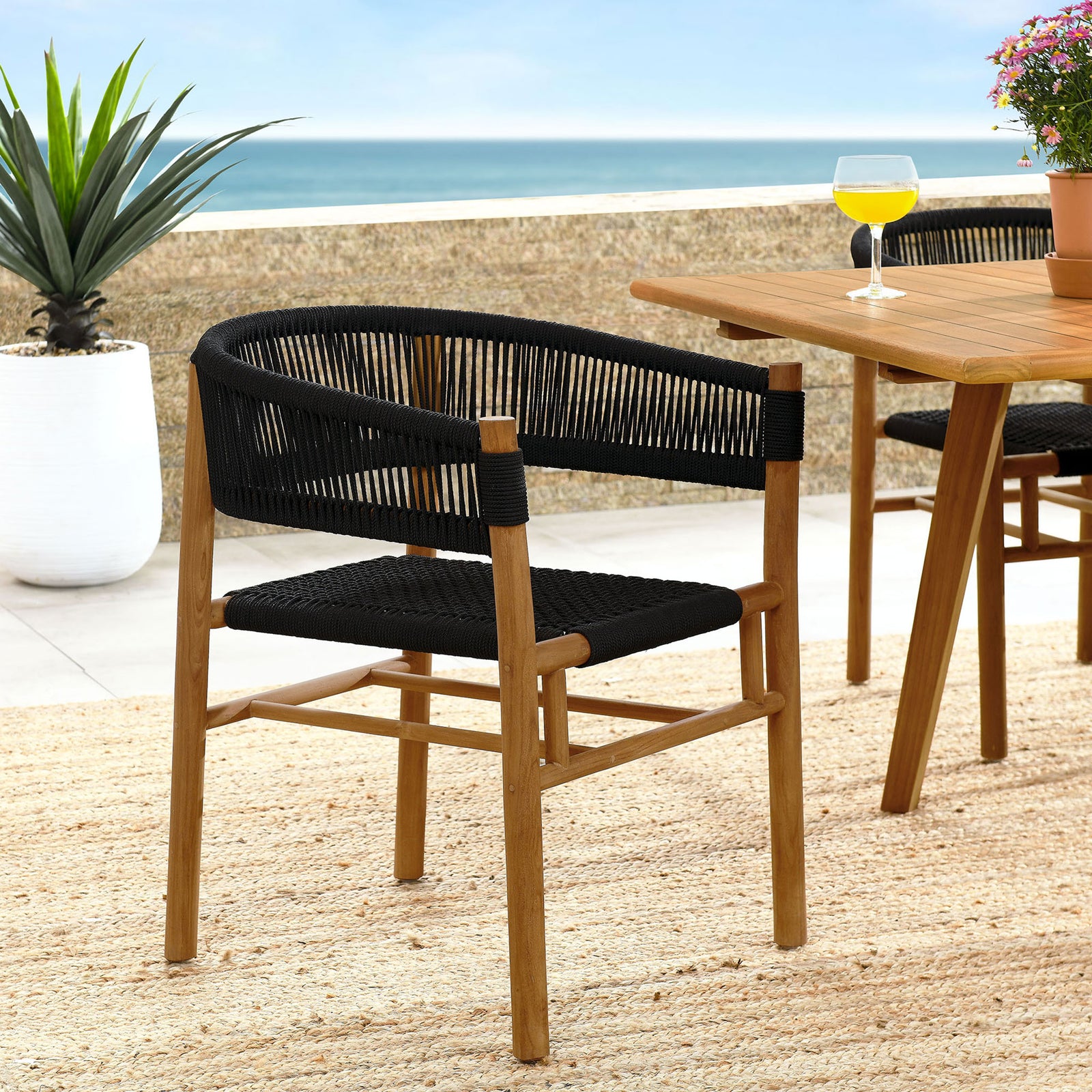 Black rope and teak dining armchair styled on a coastal patio with matching teak table and rug || EEI-6811-NAT-BLK || front_angle_room