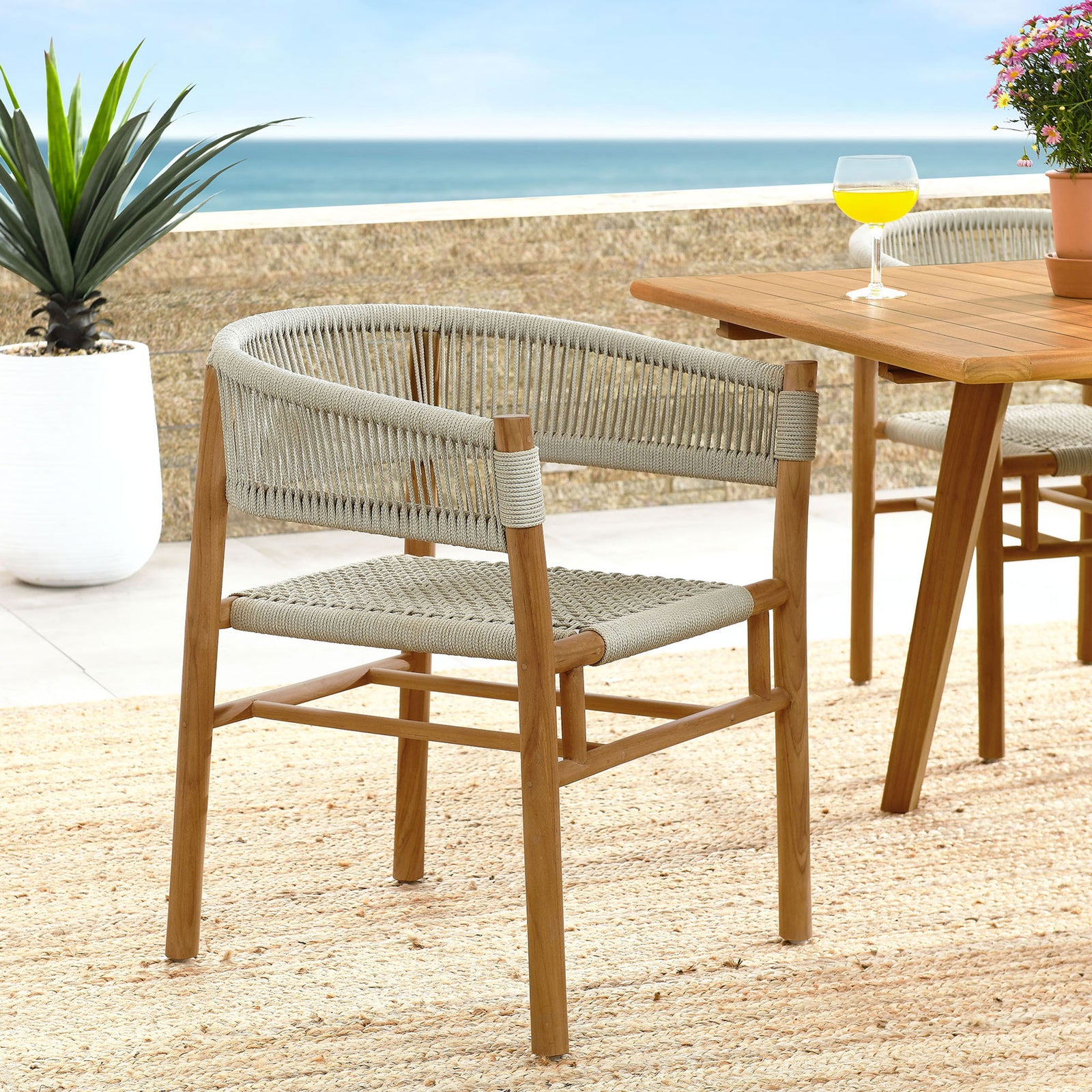 Natural rope and teak dining armchair arranged on a coastal patio with matching teak table and rug || EEI-6811-NAT-NAT || front_angle_room