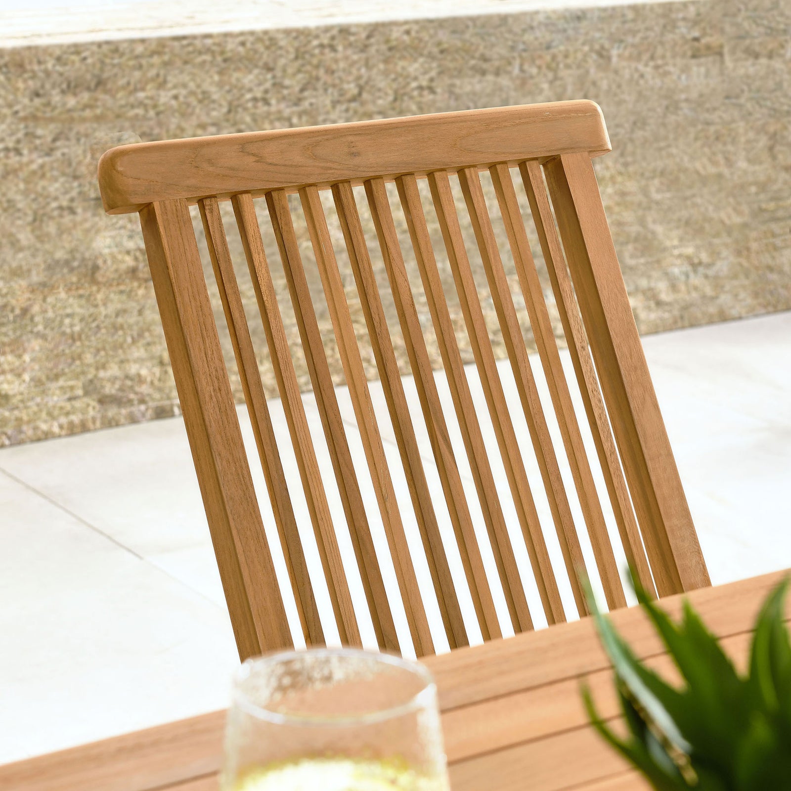 Detail of teak chair backrest on sunny patio, highlighting slim vertical slats and rounded top rail || EEI-6812-NAT || detail_room