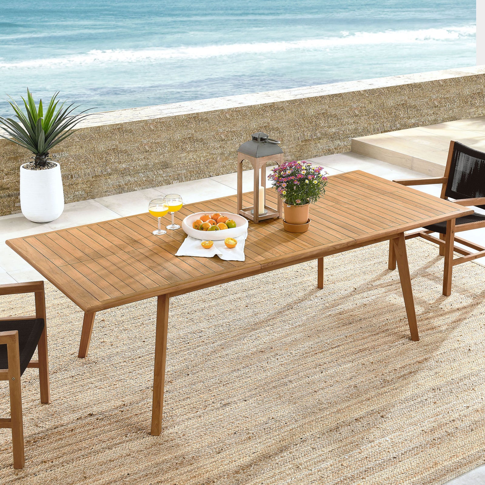 Vienna natural teak extendable patio dining table styled for coastal outdoor dining with chairs and decor. || EEI-6813-NAT || front_angle_room